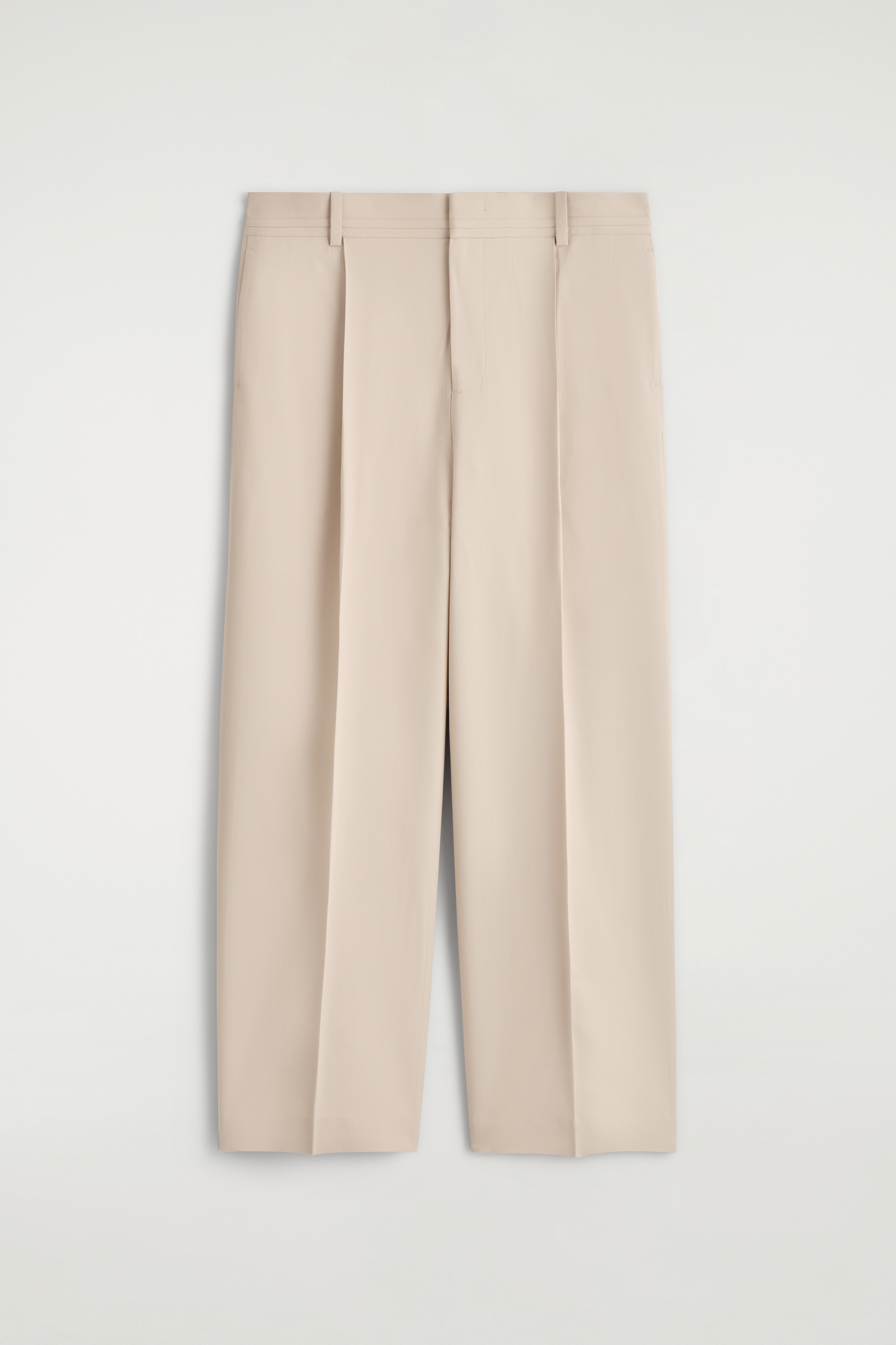 Grösseres Bild ansehen: Ein Paar hellbeige Hosen zeigt seine Vorderansicht, flach hingelegt. Es verfügt über einen flachen Bund mit Gürtelschlaufen, doppelte Falten an jedem vorderen Bein und gebügelte Bügelfalten, die bis zu den breiten, gekürzten Säumen verlaufen.