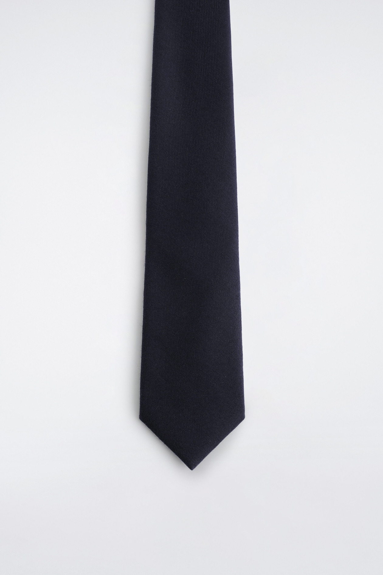 A solid navy blue necktie hanging vertically in a front view, showcasing a textured, matte-finished fabric and a classic pointed tip.