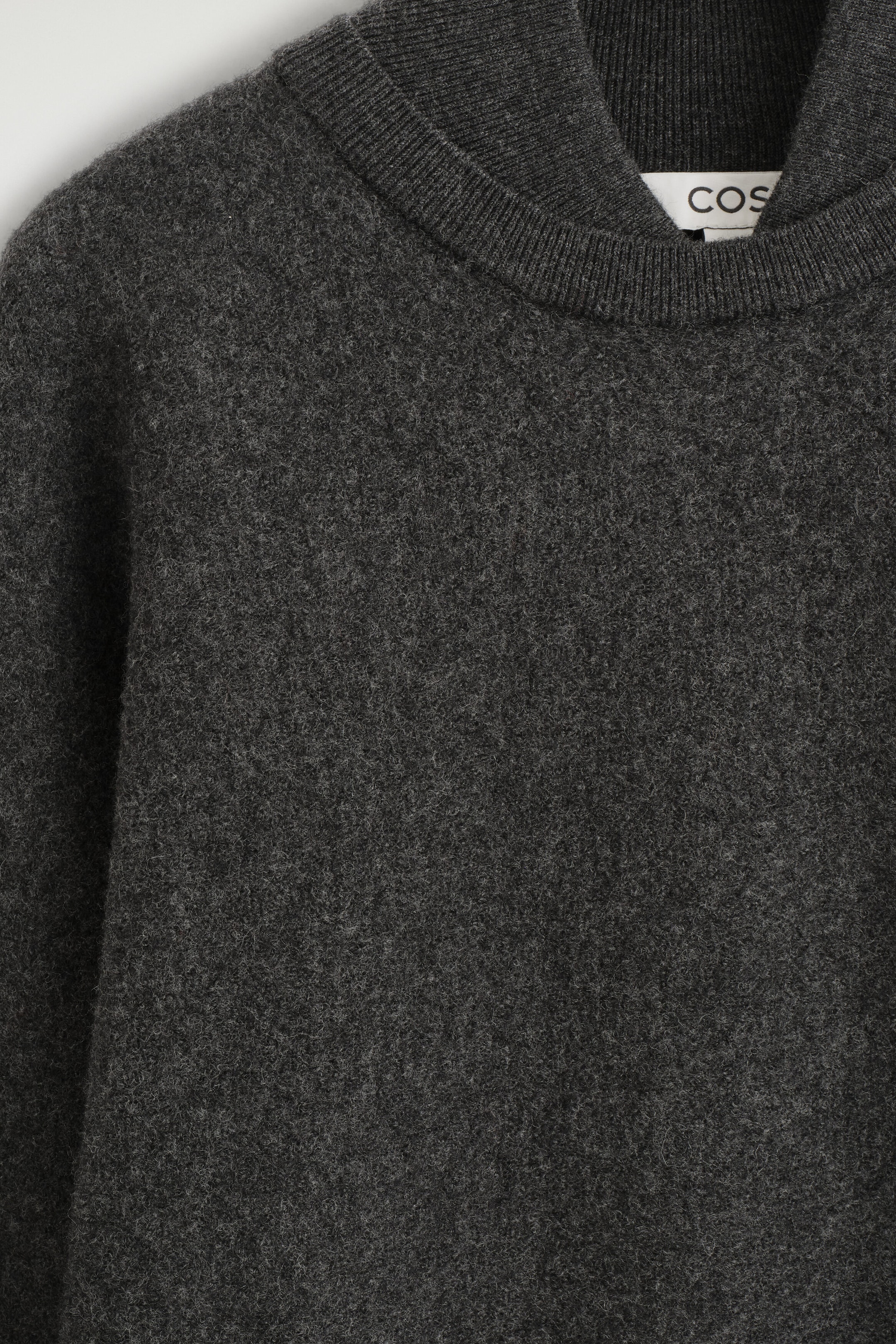 The layered-collar boiled wool jumper features a textured dark gray fabric with a distinctive double-layered neckline. This front close-up highlights the outer ribbed crew neck collar layered over an inner ribbed collar.