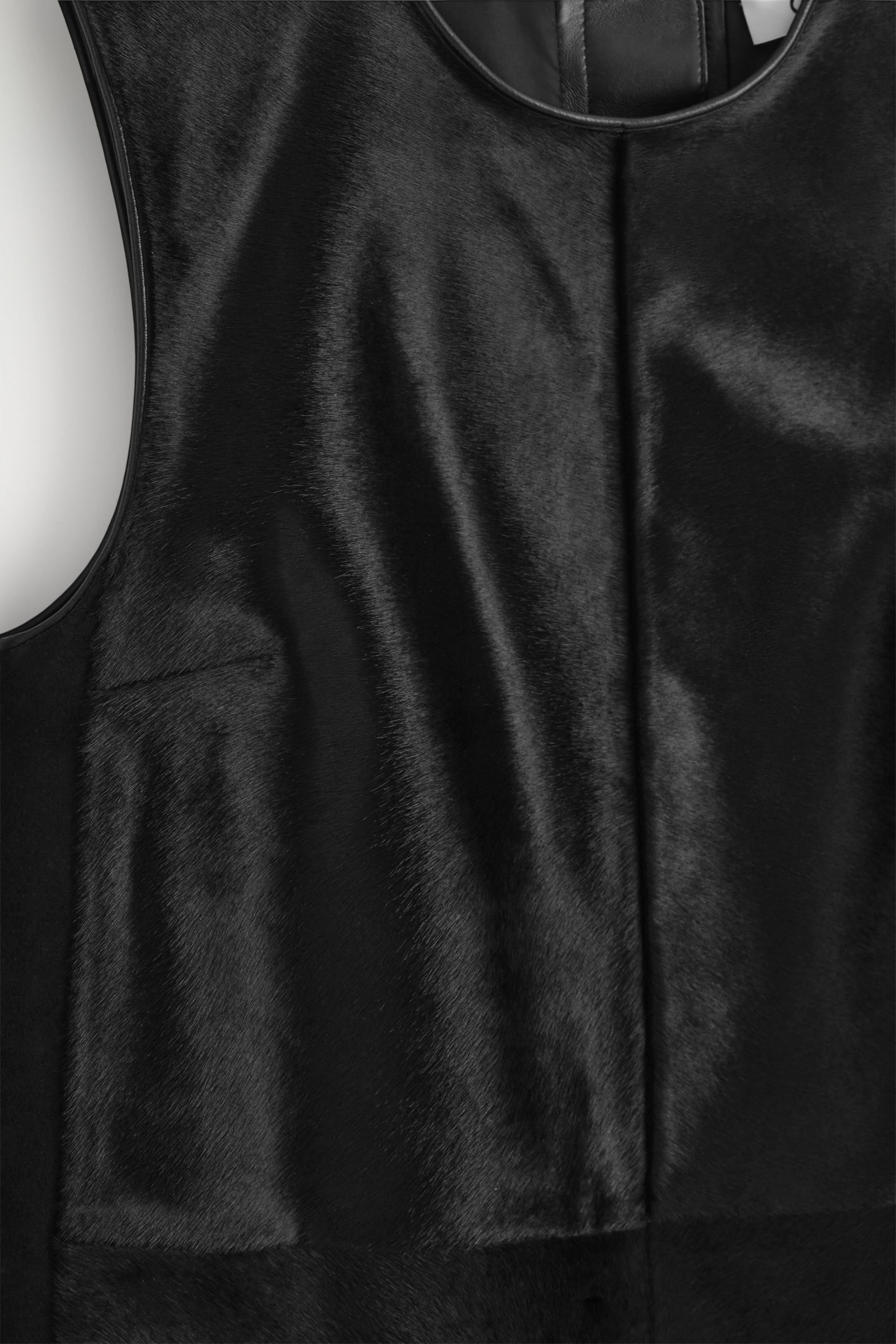 Agrandir l'image: Une robe droite noire est présentée de FACE, fabriquée en cuir de poulain brillant, avec des empiècements ton sur ton et des bords en cuir collé visibles autour de l'encolure et des emmanchures.