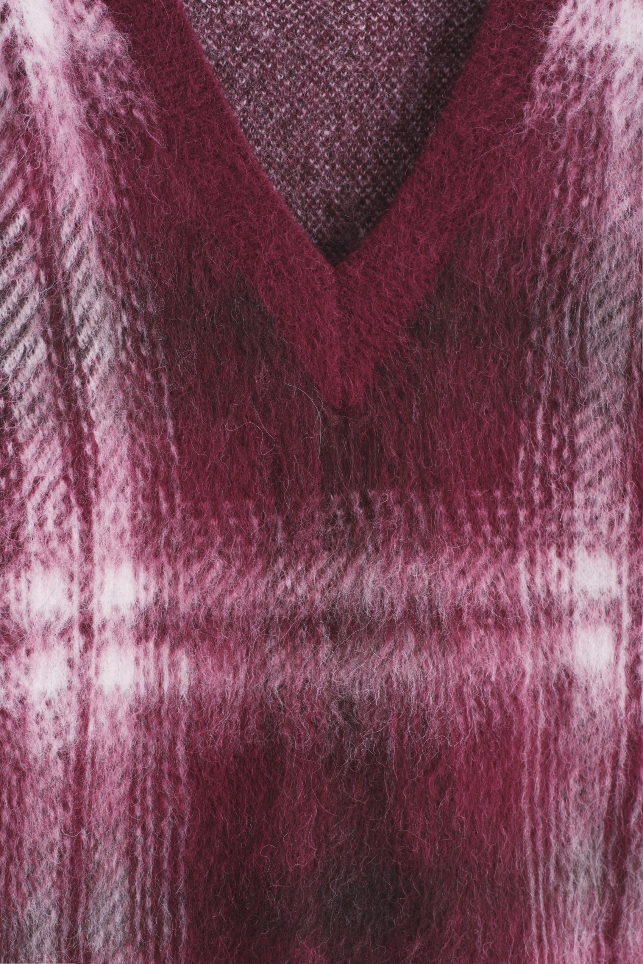 Grösseres Bild ansehen: Ein gestrickter V-Ausschnitt-Pullover präsentiert eine Vorderansicht und zeigt ein flauschiges Karomuster in Schattierungen von Magenta und Burgunderrot mit helleren rosa und weißen Linien. Eine feinere Stricktextur ist im Inneren des V-Ausschnitts sichtbar.