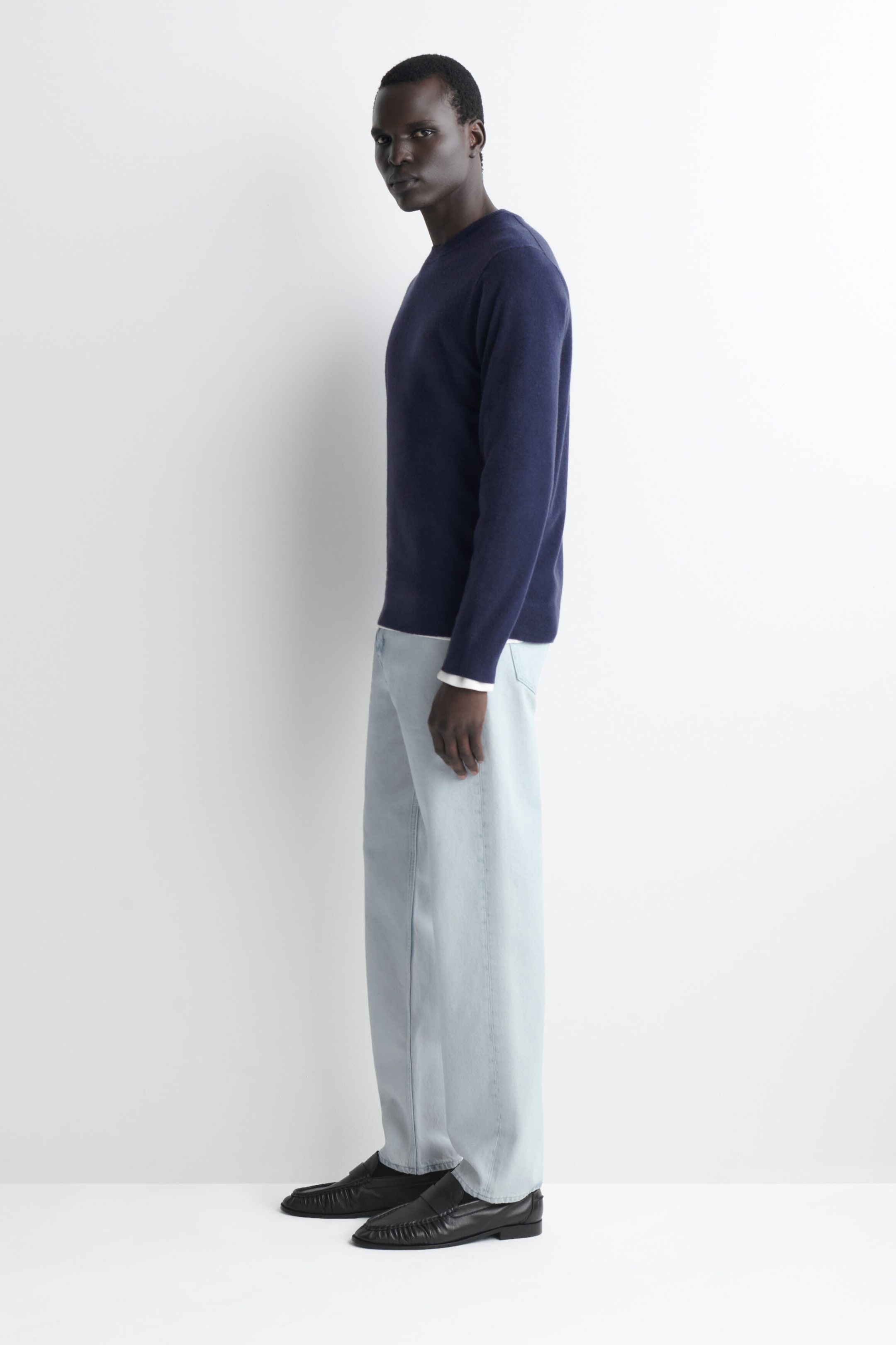 A navy blue cashmere crew neck jumper is shown from a left-facing profile, highlighting its straight fit and fine-knit texture. The jumper features a classic crew neckline and long sleeves, with a hint of a white shirt sleeve peeking out from the cuff. A navy blue cashmere crew neck jumper is shown from a left-facing profile, highlighting its straight fit and fine-knit texture. The jumper features a classic crew neckline and long sleeves, with a hint of a white shirt sleeve peeking out from the cuff.
