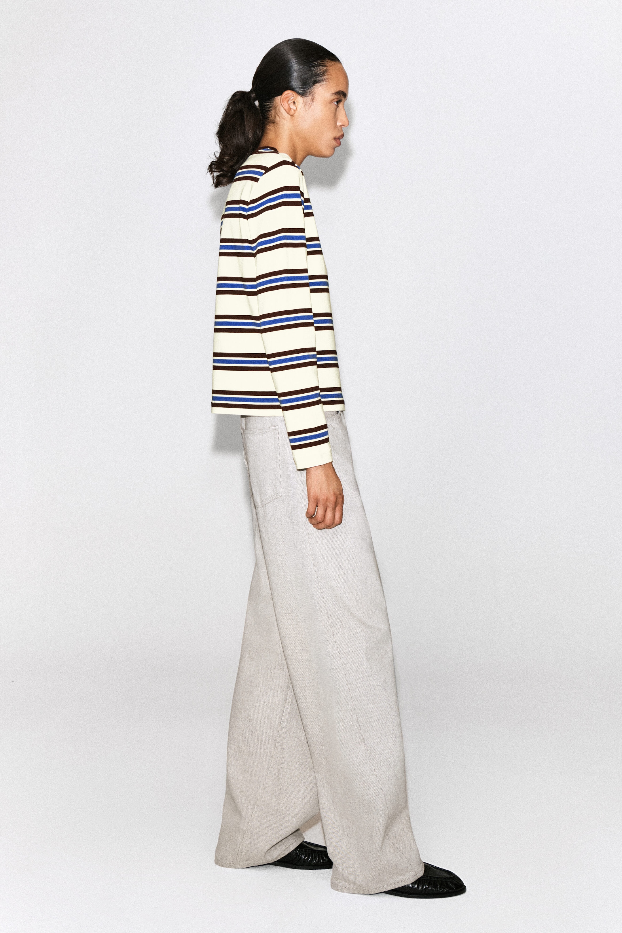 The clean-cut long-sleeved T-shirt displays horizontal stripes in cream, brown and blue, shown from a side profile facing right to highlight its relaxed, boxy fit. It features long sleeves and a straight, clean-cut hemline that rests over light-coloured wide-leg trousers. The clean-cut long-sleeved T-shirt displays horizontal stripes in cream, brown and blue, shown from a side profile facing right to highlight its relaxed, boxy fit. It features long sleeves and a straight, clean-cut hemline that rests over light-coloured wide-leg trousers.