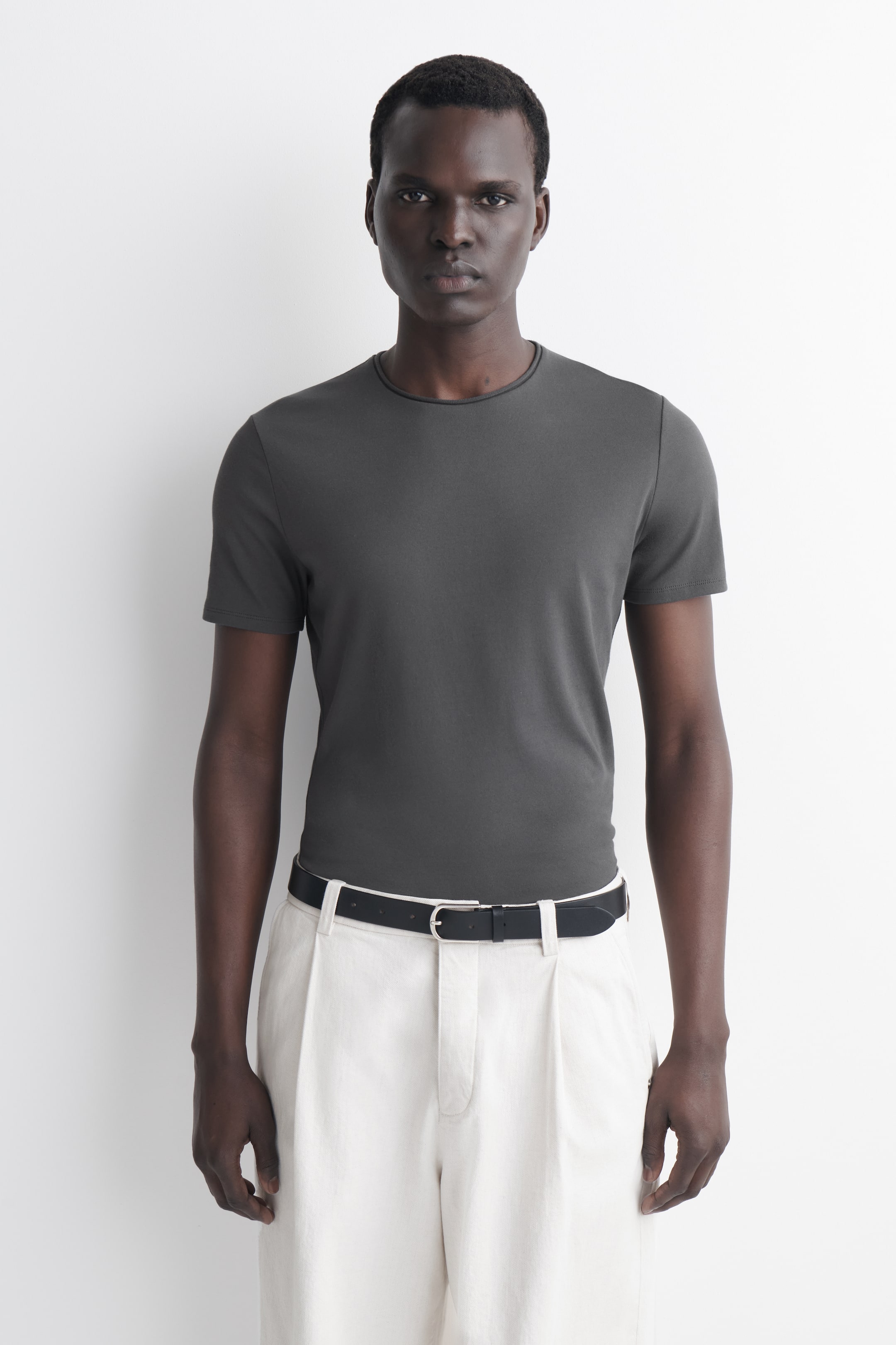 Größeres Bild ansehen: Ein dunkelgraues T-Shirt wird von vorne gezeigt, mit einer schmalen Passform, kurzen Ärmeln und einem gerollten Rundhalsausschnitt.