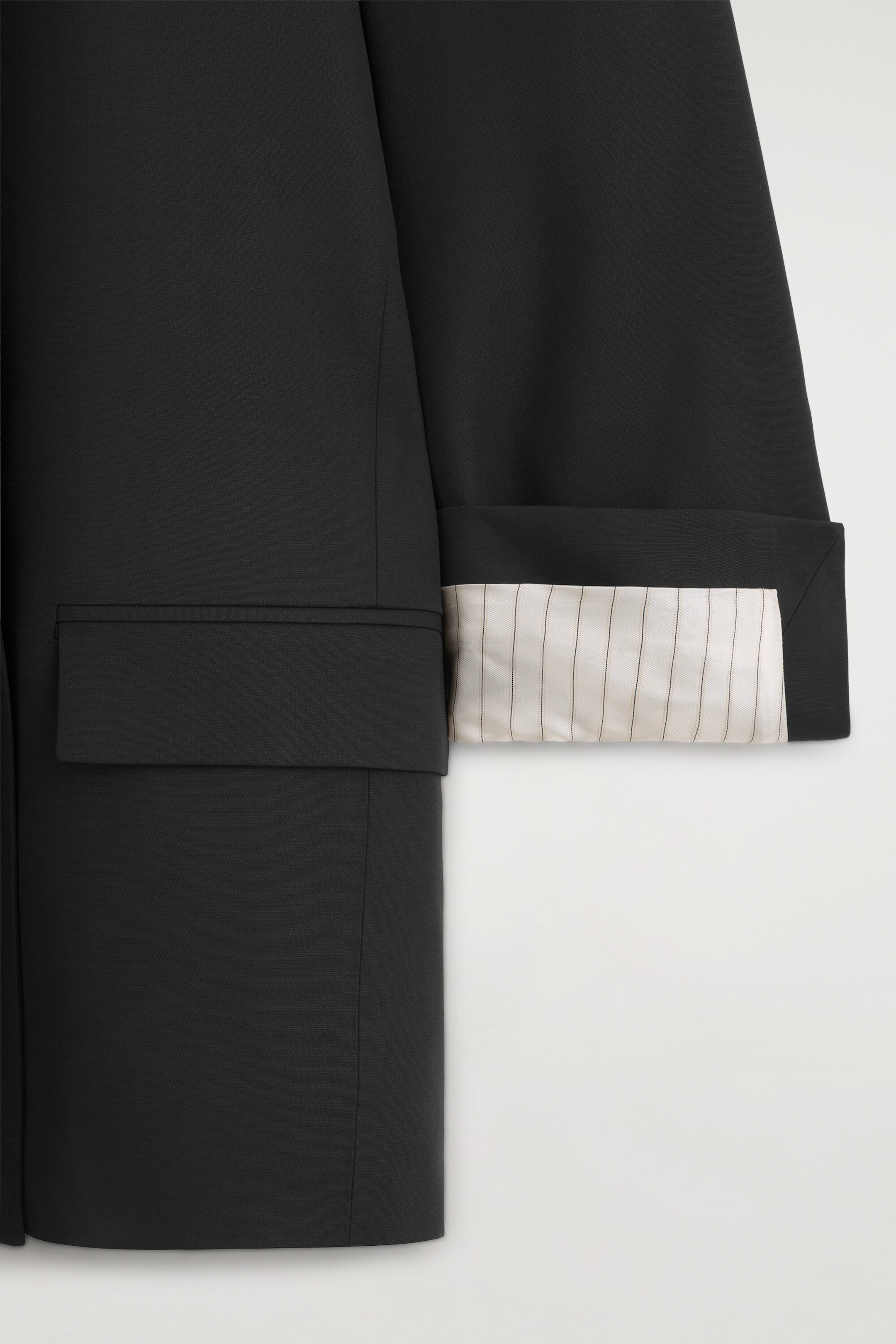Ce gros plan du blazer croisé noir à passepoil contrastant met en valeur une poche à rabat structurée sur le côté. Le revers du poignet de manche est replié, révélant une doublure contrastante de couleur claire avec de fines rayures verticales façon craie.