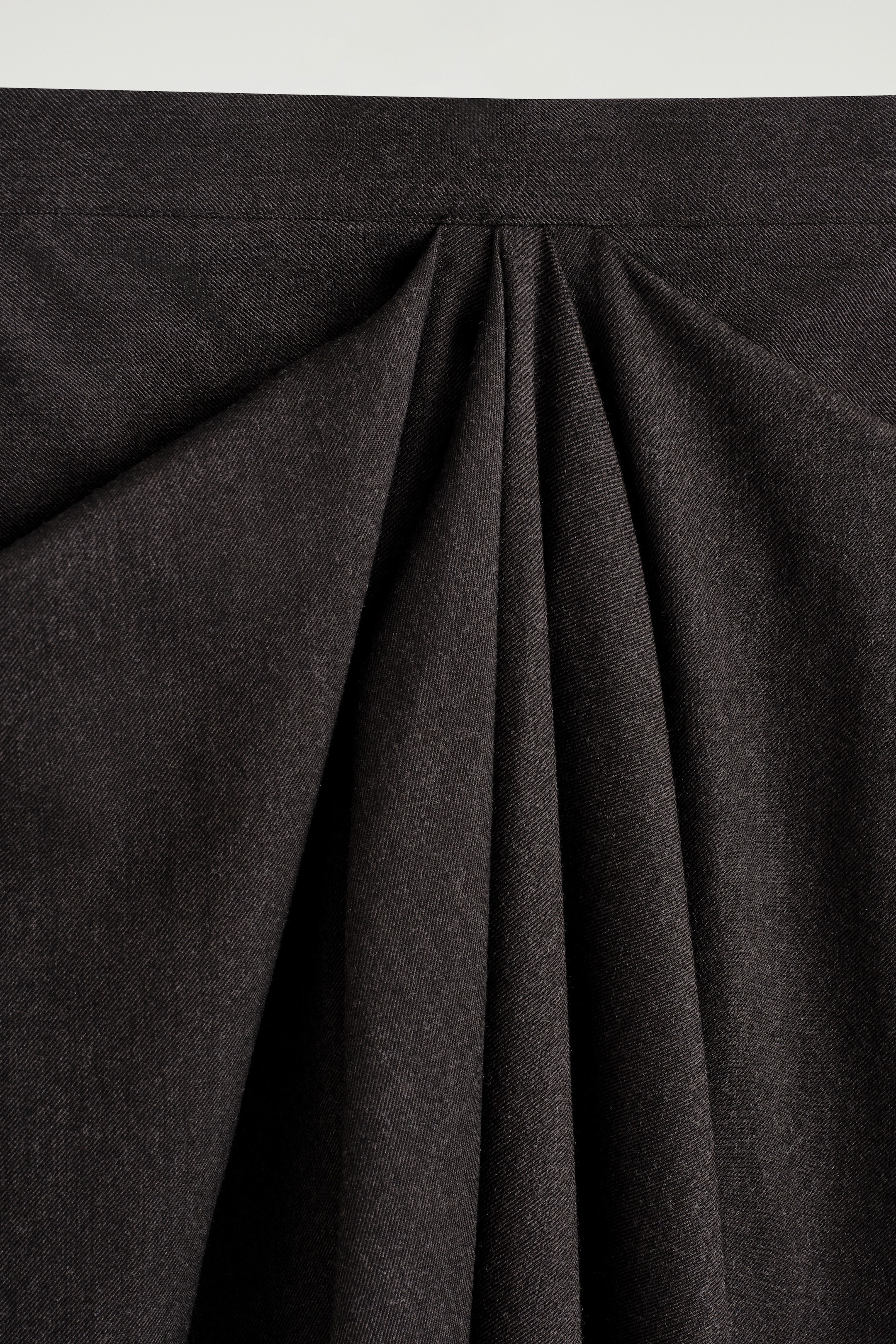 Nagyobb kép megtekintése: A DRAPED WOOL-BLEND MIDI SZOKNYA elölről van bemutatva, sötétszürke anyaggal, amely finom textúrával rendelkezik. Mély, puha redők indulnak ki egy lapos derékpántból, lefelé áramlanak, és jelentős volument hoznak létre.