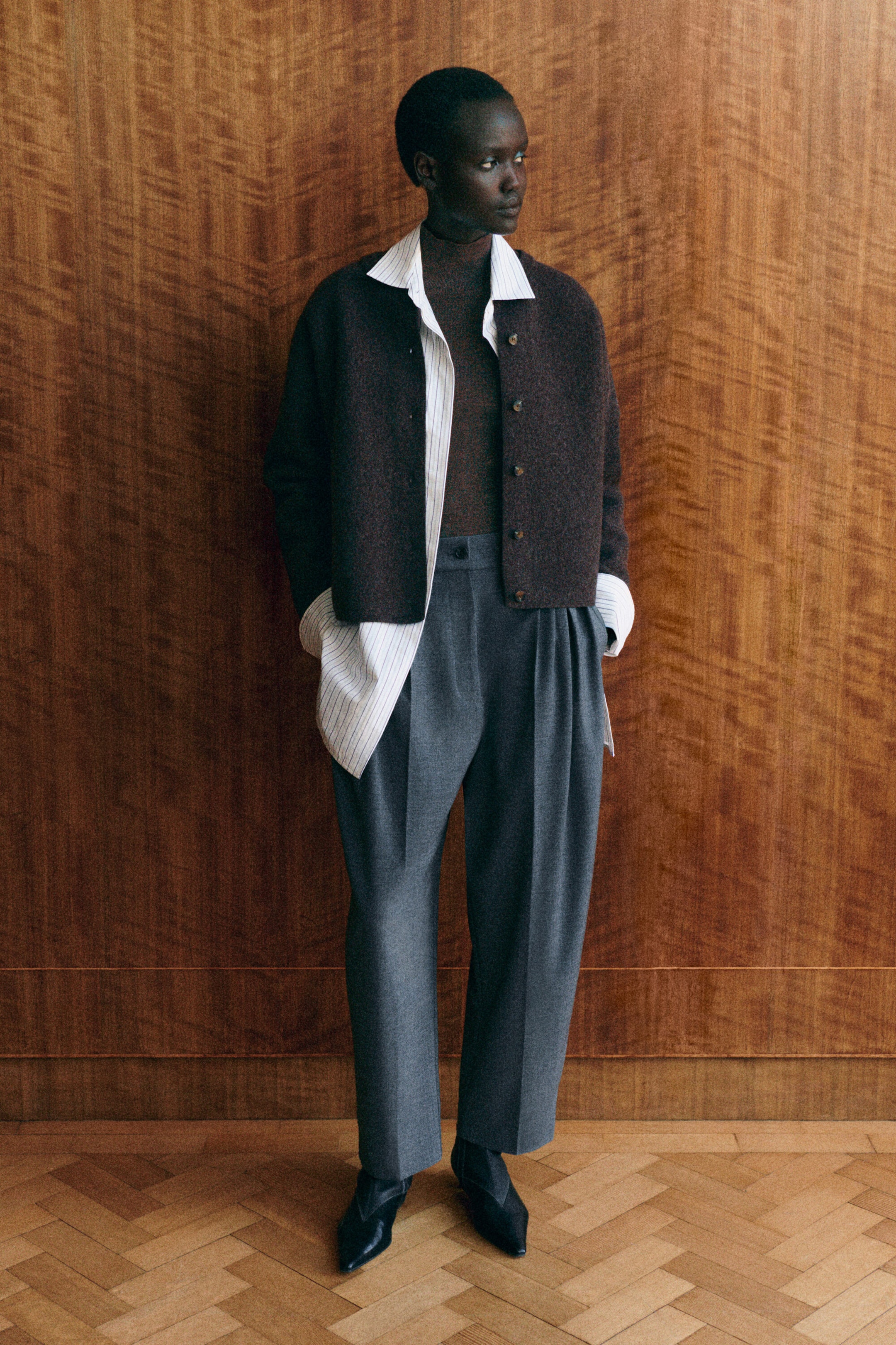 Eine dunkelbraune Strickjacke aus Walkwolle ist von vorne zu sehen, mit weich gerundeter Silhouette, ohne Kragen und mit durchgehender Knopfleiste. Die Strickjacke wird in einer Lagenkombination über einem gestreiften Hemd mit Knopfleiste und einem braunen Rollkragen-Optik-Top getragen und zeigt ihre lockere Passform. Eine dunkelbraune Strickjacke aus Walkwolle ist von vorne zu sehen, mit weich gerundeter Silhouette, ohne Kragen und mit durchgehender Knopfleiste. Die Strickjacke wird in einer Lagenkombination über einem gestreiften Hemd mit Knopfleiste und einem braunen Rollkragen-Optik-Top getragen und zeigt ihre lockere Passform.