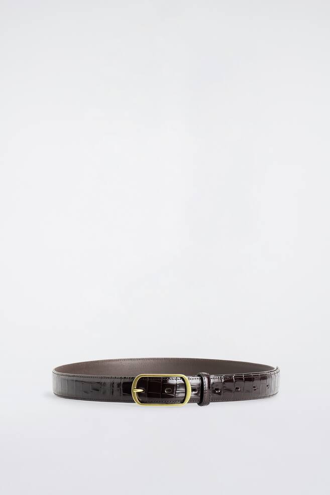 La ceinture en cuir Ã  boucle incurvÃ©e repose en boucle fermÃ©e, mettant en valeur sa sangle en cuir brun foncÃ© embossÃ©e faÃ§on crocodile, avec une finition brillante. Elle prÃ©sente Ã  lâavant une boucle rectangulaire arrondie de ton dorÃ©, avec une seule ardillon, ainsi quâun passant assorti en cuir. - 1