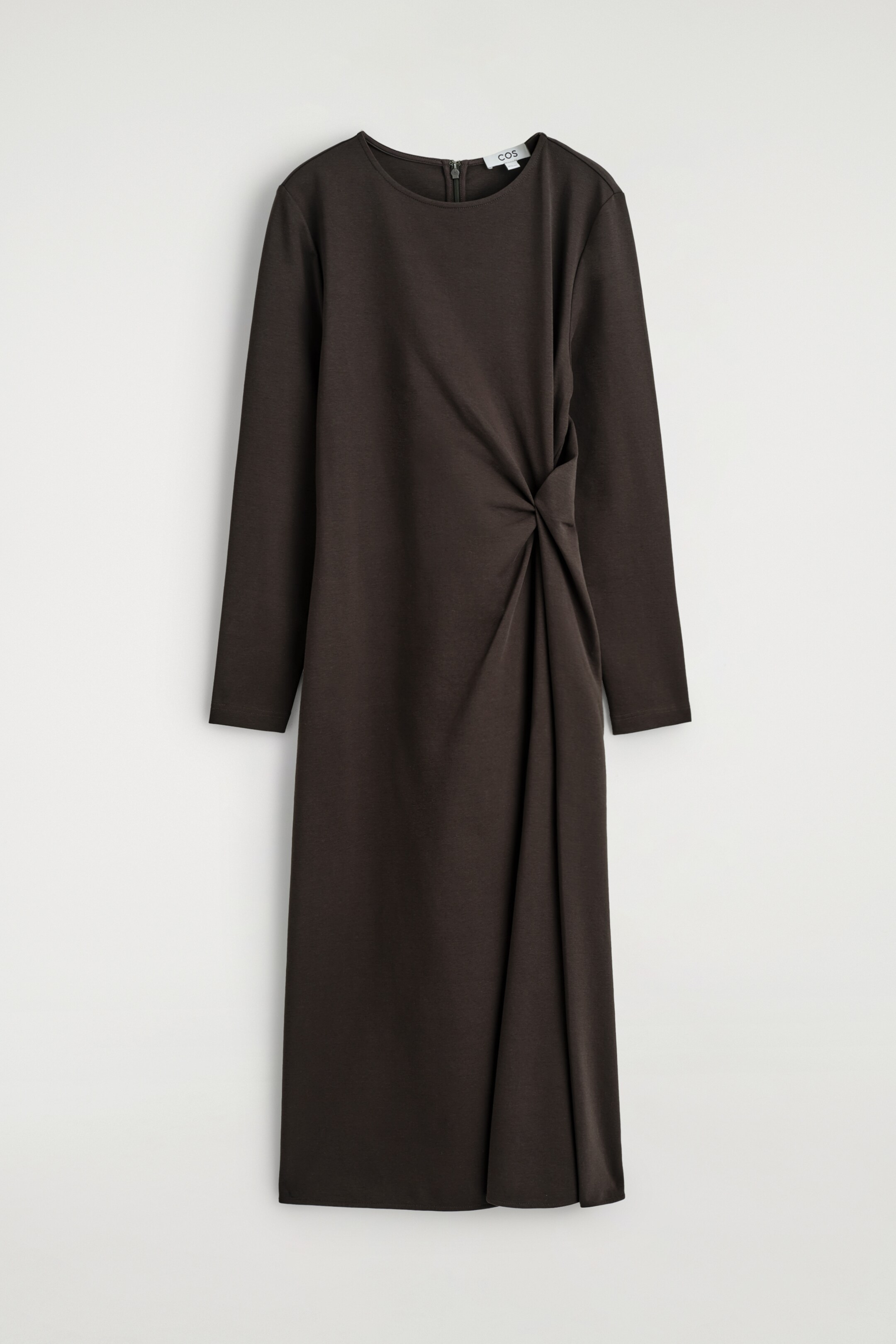 Agrandir l'image: Une robe mi-longue marron foncé est tournée vers l'AVANT, avec des manches longues et un col rond. Un détail de nœud torsadé est visible sur le côté gauche de la taille, créant un effet drapé sur le bas de la jupe.