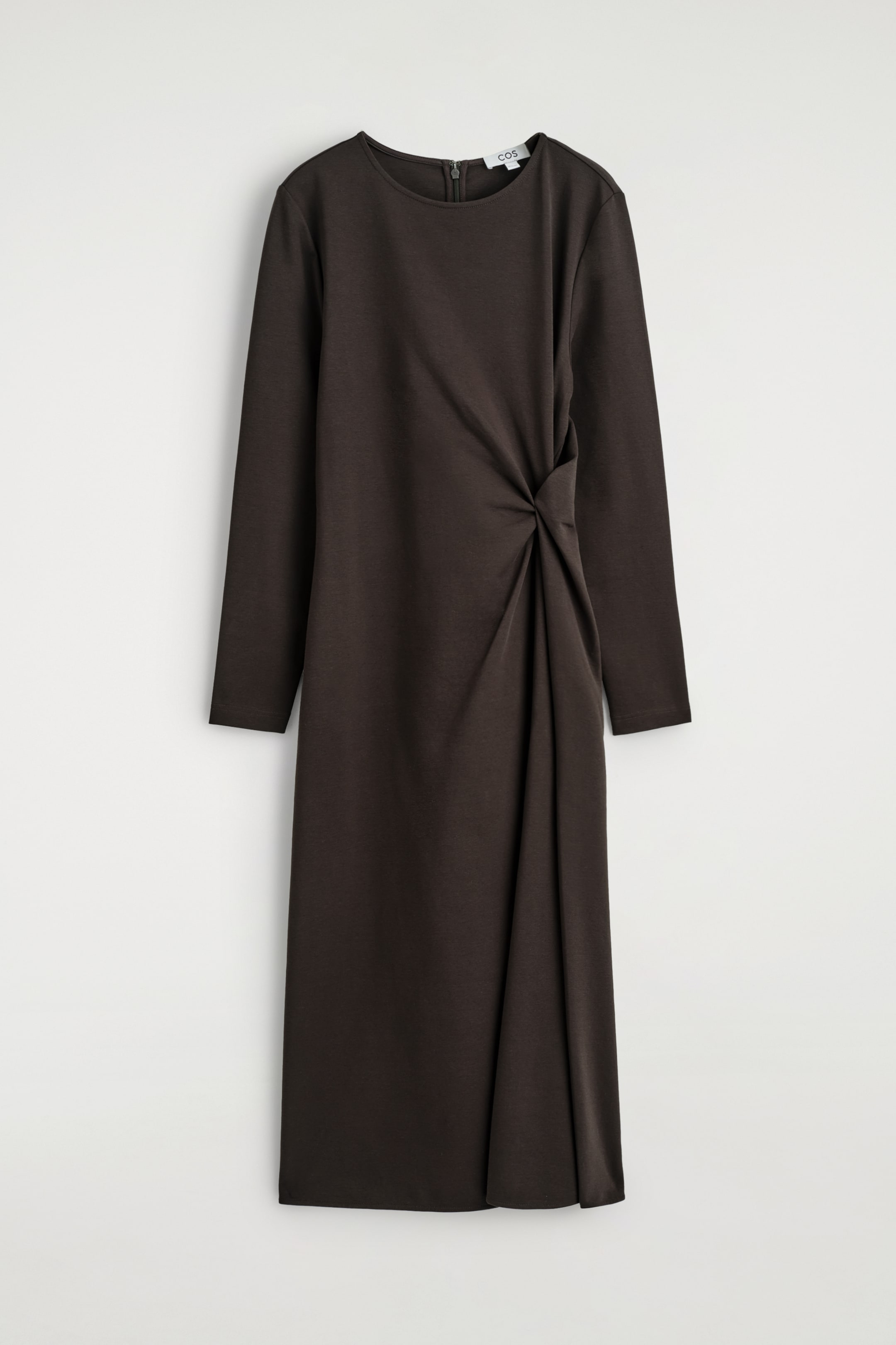 Agrandir l'image: Une robe mi-longue marron foncé est tournée vers l'AVANT, avec des manches longues et un col rond. Un détail de nœud torsadé est visible sur le côté gauche de la taille, créant un effet drapé sur le bas de la jupe.