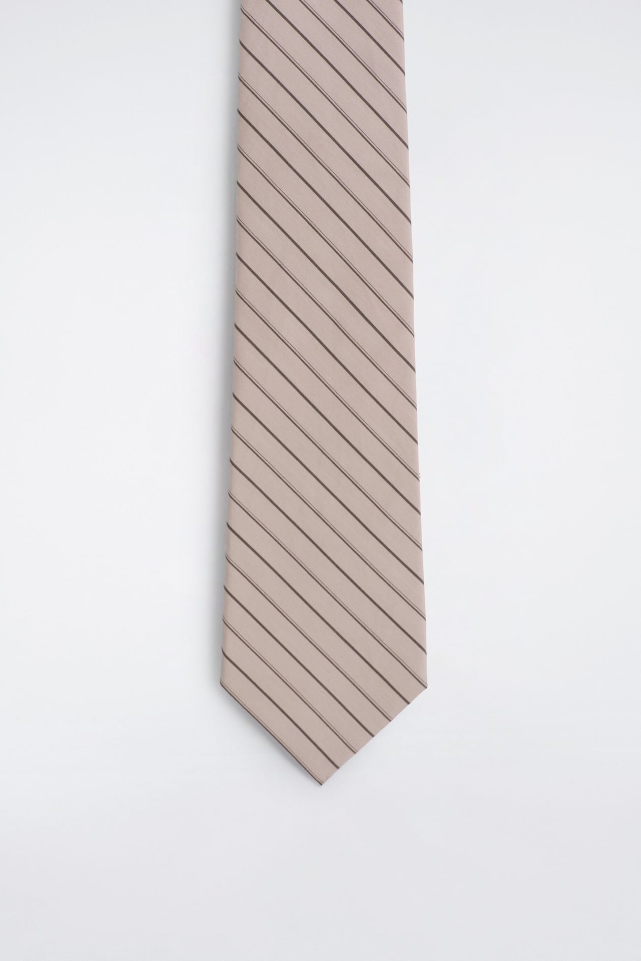 En slips visas i frontvy med en ljus taupefärgad bas och smala, mörkbruna diagonala ränder. Slipsen smalnar av ned mot en klassisk spetsig ände längst ner.