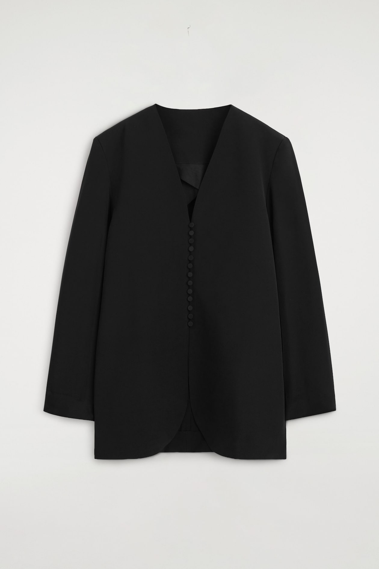 Ein schwarzer Blazer ohne Kragen ist von vorne dargestellt und verfügt über einen tiefen V-Ausschnitt sowie einen mittigen Verschluss mit einer vertikalen Reihe kleiner, mit Stoff bezogener Knöpfe. Die langärmelige Jacke hat eine strukturierte, schmale Silhouette mit einem leicht geschwungenen vorderen Saum.