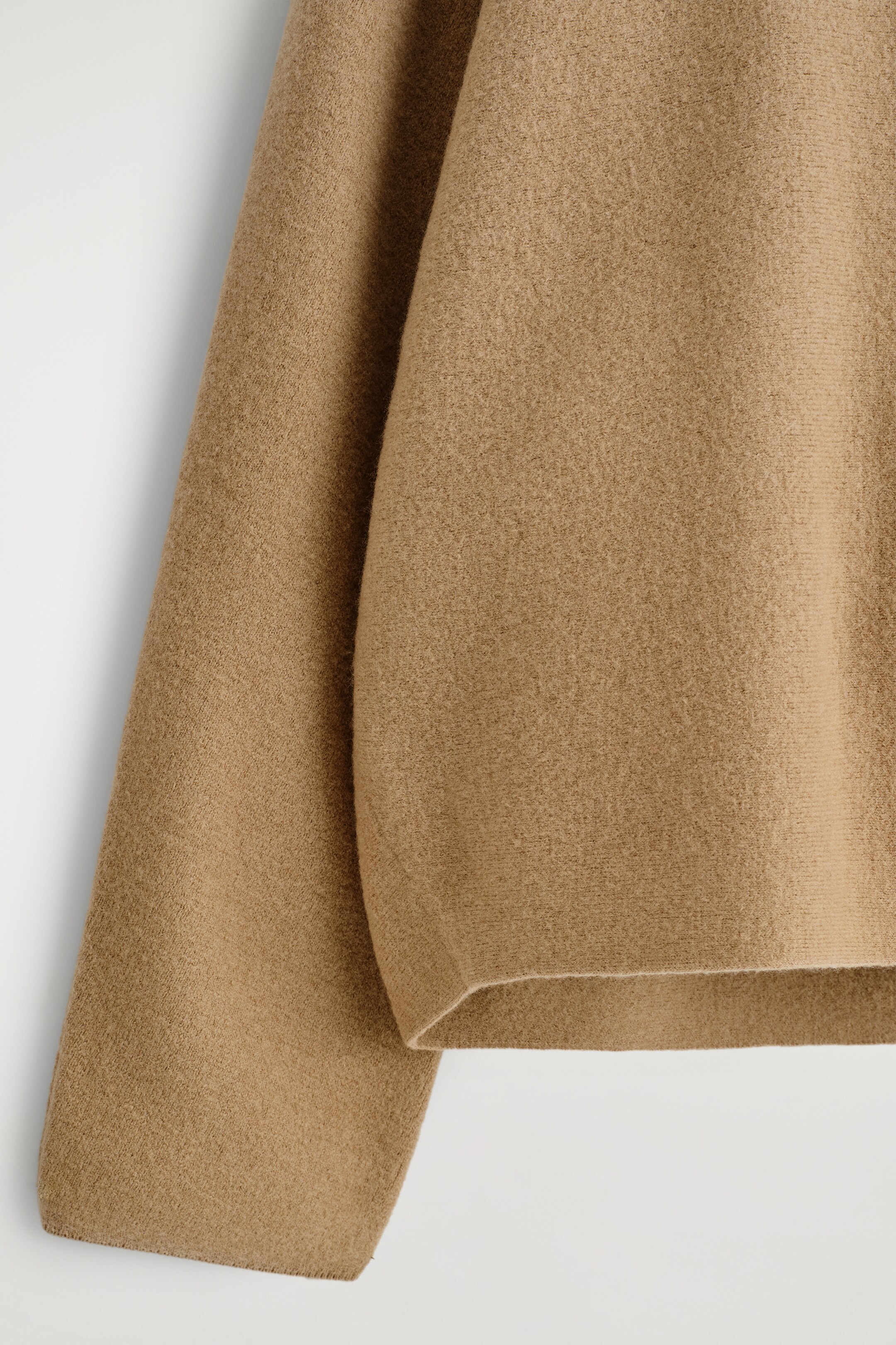 Ver imagen más grande: El jersey de punto color camel muestra una superficie texturizada de lana merino hervida en una vista de primer plano. Una manga ancha se extiende a la izquierda, y el cuerpo de la prenda presenta un dobladillo limpio y acabado a la derecha.