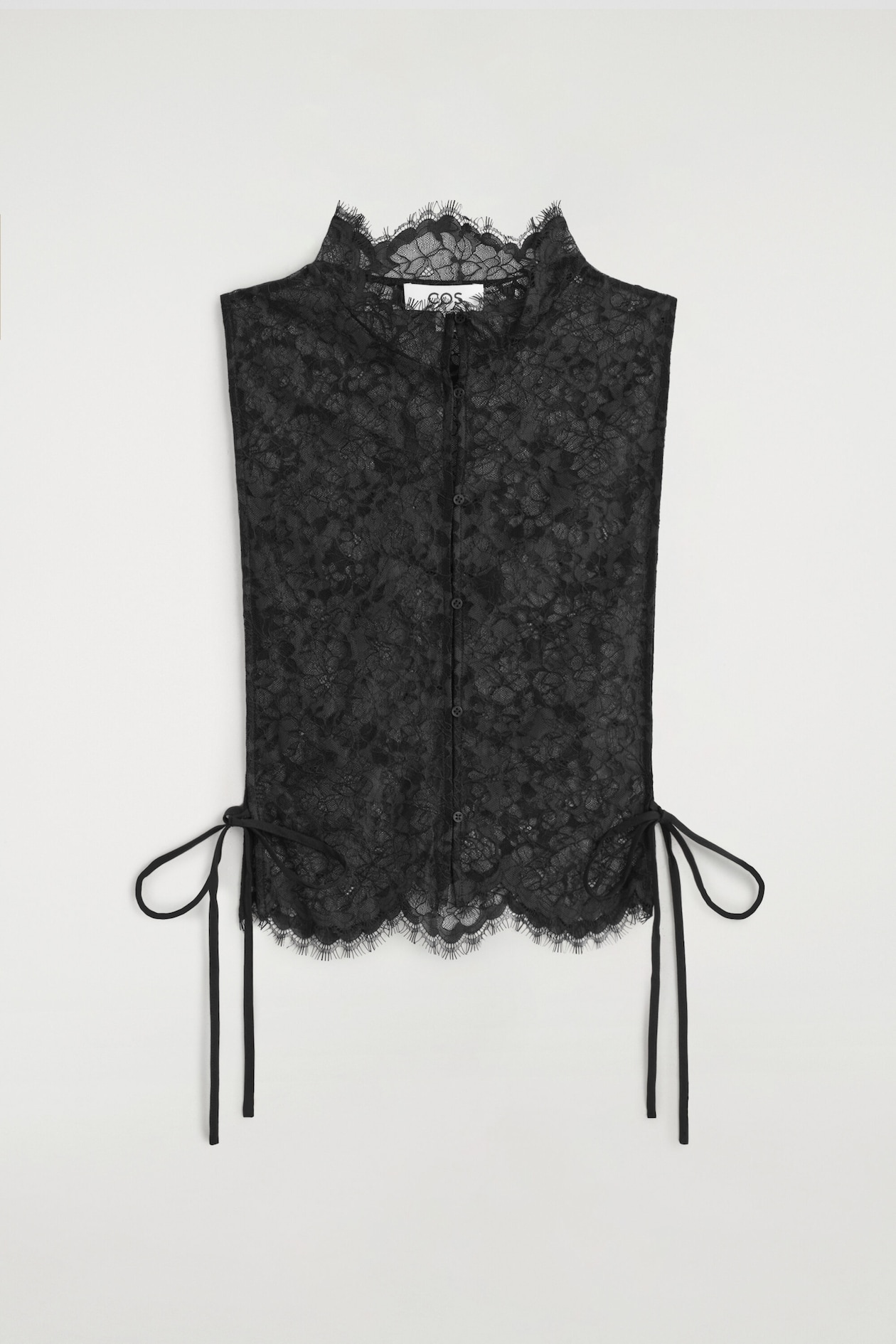 A black scalloped lace bib is facing forward, showcasing its sheer floral lace construction and a high, scalloped mock-neck collar. The bib features a central button-down closure and thin side-tie straps that fasten the open sides.