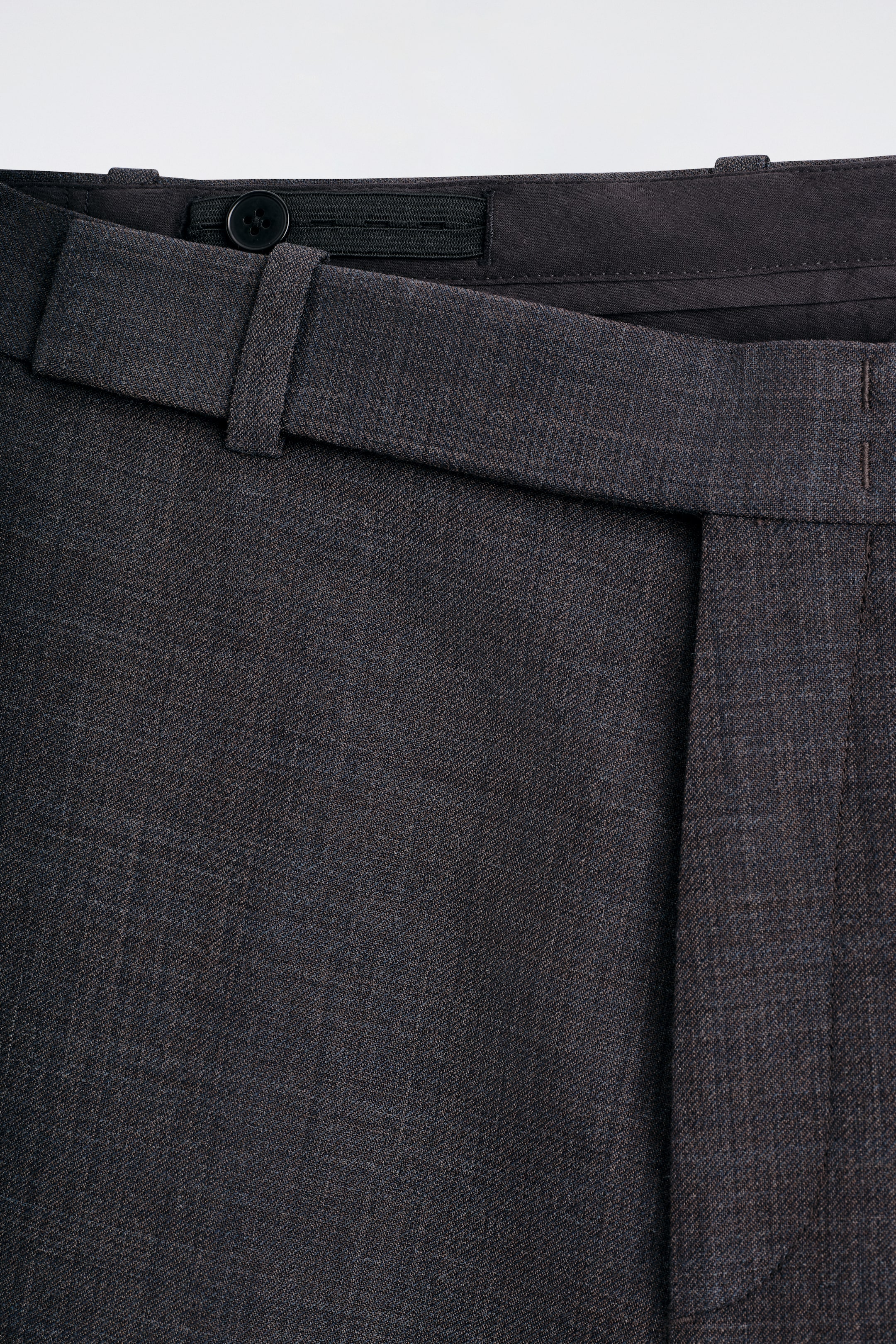 Agrandir l'image: Vue de face d'un pantalon en charbon foncé, avec un tissu texturé, une ceinture visible avec un bouton intérieur et une fermeture élastique, ainsi qu'un pli vertical prononcé.