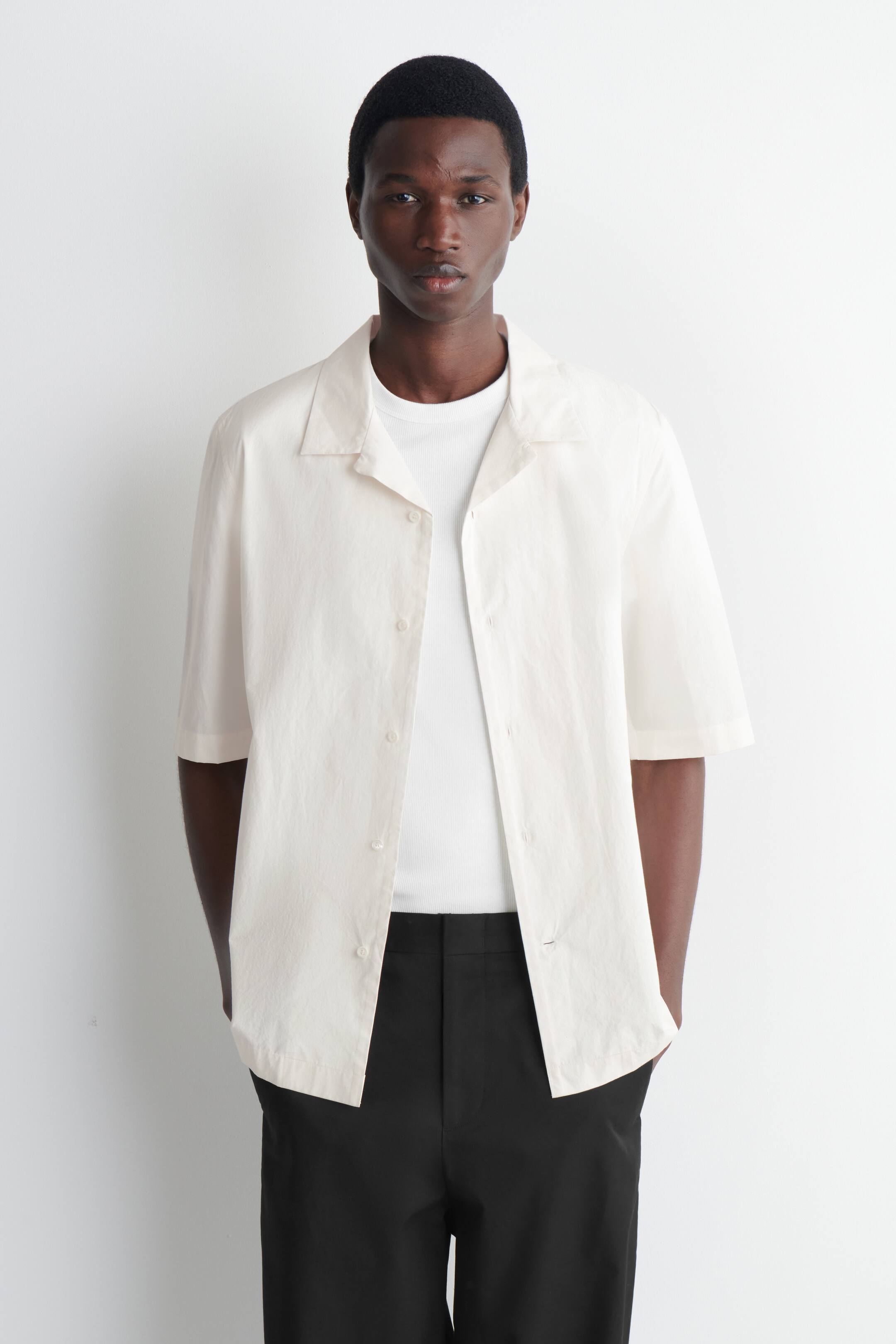 Näytä suurempi kuva: Off-white lyhythihainen paita esitellään edestäpäin, ja siinä on leirityylinen kaulus sekä avoin nappikiinnitys vaaleilla napeilla. Se on rento malli kevyestä kankaasta, ja sitä käytetään valkoisen ribatun t-paidan ja mustien housujen päällä.