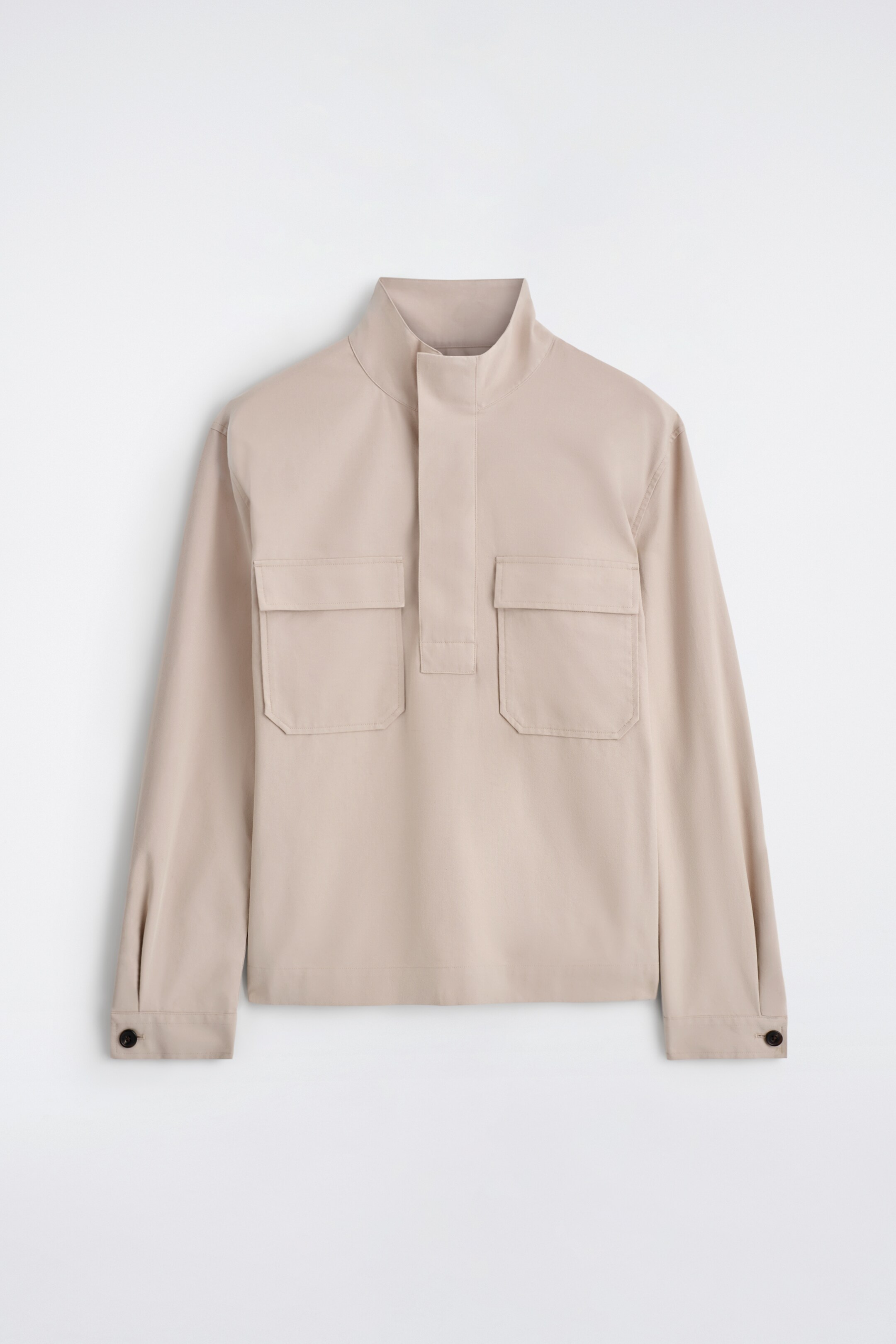 Ver imagen más grande: Una camisa de color beige claro se presenta desde el frente. Cuenta con un cuello tipo embudo, una pieza central con media cremallera y dos bolsillos de parche rectangulares en el pecho. Sus mangas largas terminan en puños con un solo botón.