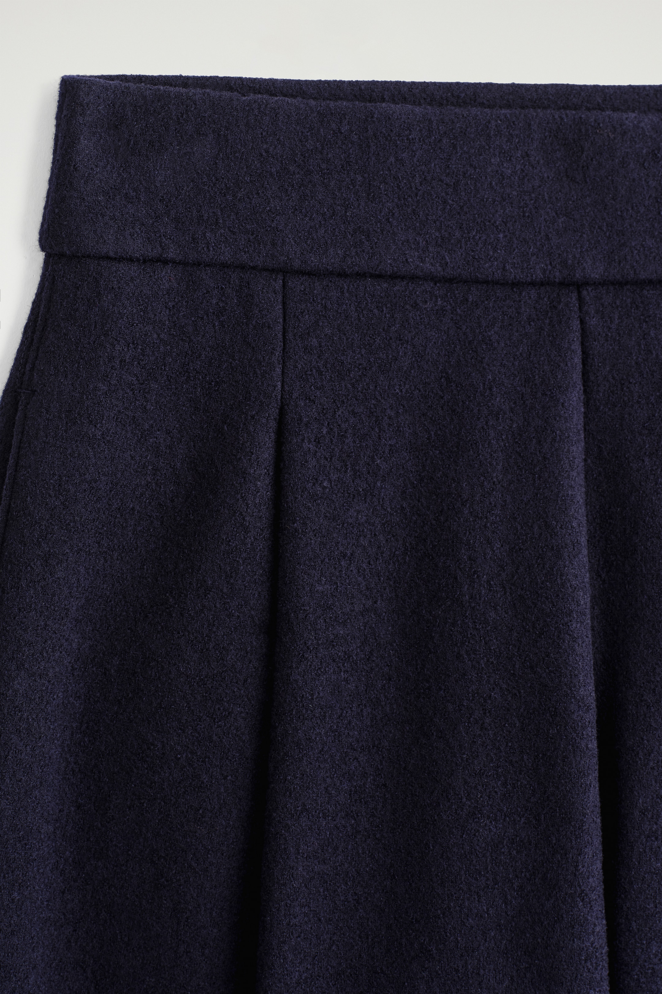 Ingrandisci l'immagine: Un indumento di colore blu navy scuro, possibilmente una gonna o pantaloni a gamba larga, presenta una fascia in vita ampia con morbide pieghe verticali che scendono da essa, tutte con una texture infeltrita.