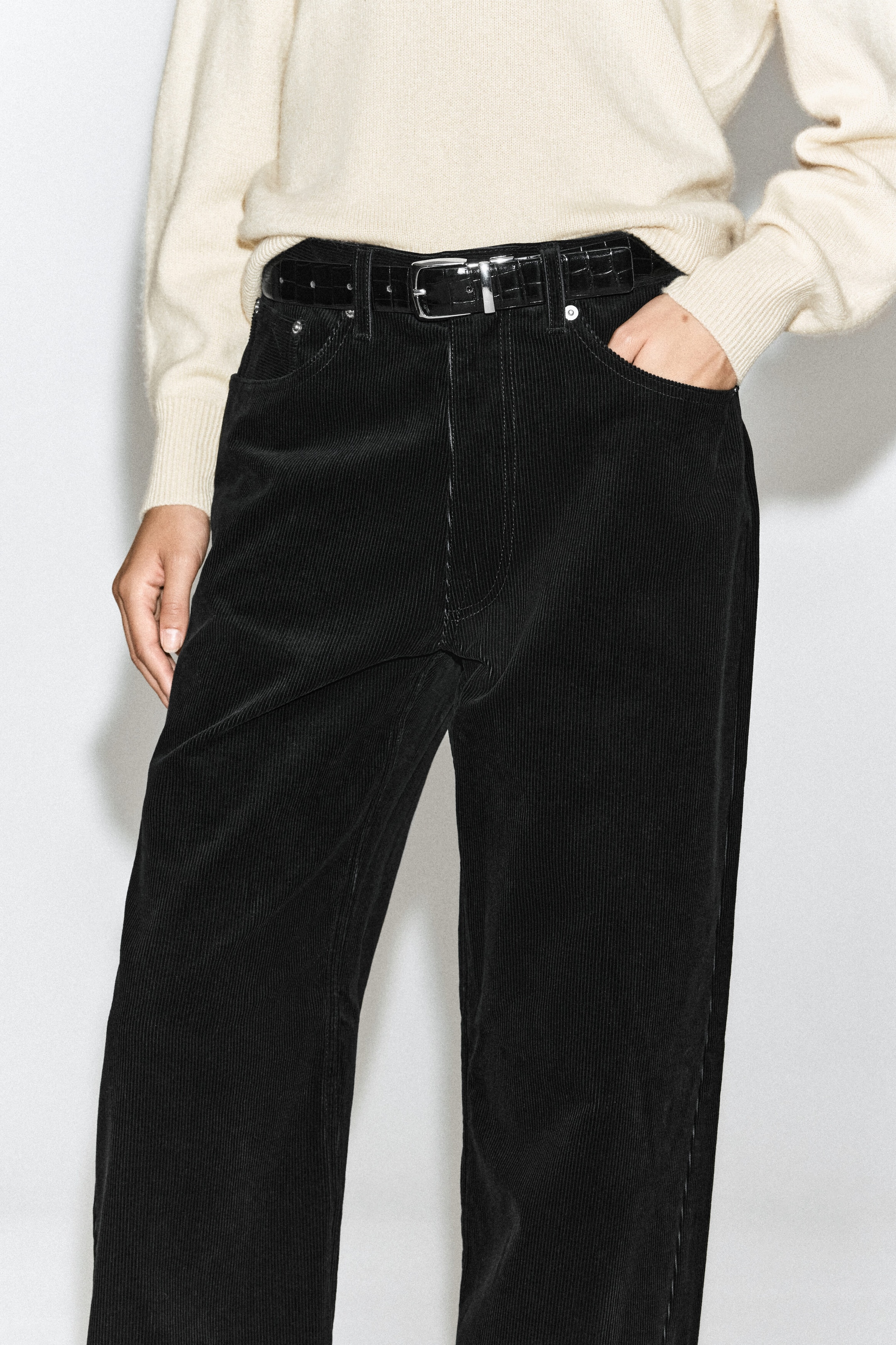 The Facade corduroy straight-leg jeans in black are being worn by the model with a tucked-in cream jumper and a black textured belt. The jeans feature a ribbed corduroy texture, belt loops, and classic front pockets, with the model resting one hand inside a pocket. The Facade corduroy straight-leg jeans in black are being worn by the model with a tucked-in cream jumper and a black textured belt. The jeans feature a ribbed corduroy texture, belt loops, and classic front pockets, with the model resting one hand inside a pocket.