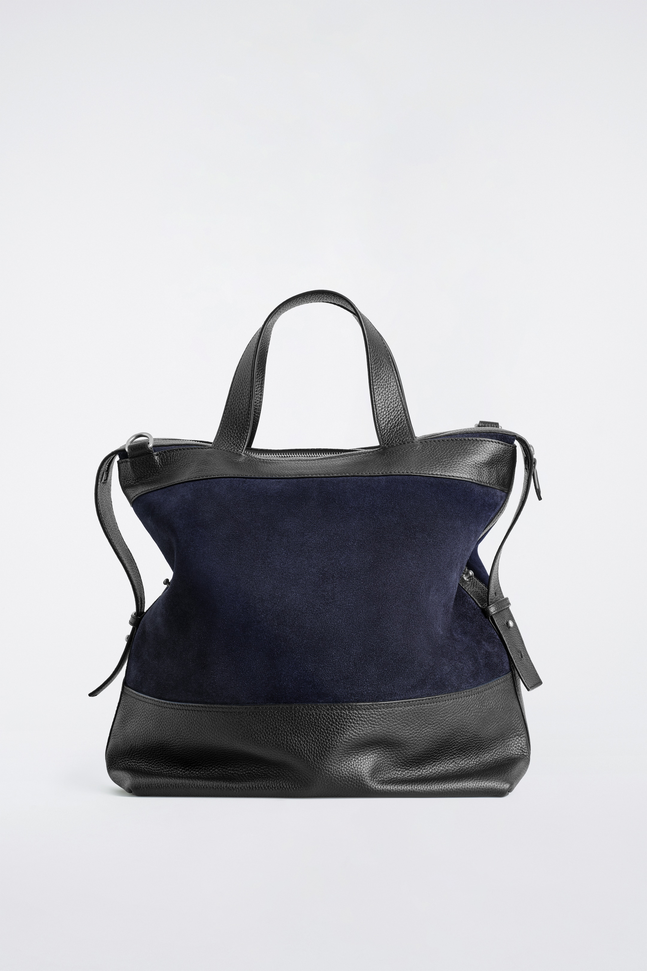 Visualizza immagine più grande: Una borsa bicolore è esposta FRONTE, con un corpo in camoscio blu scuro e rifiniture superiori in pelle nera a grana, manici superiori e base. È progettata con una chiusura a zip lungo l'apertura superiore e una tracolla staccabile appesa ai lati.