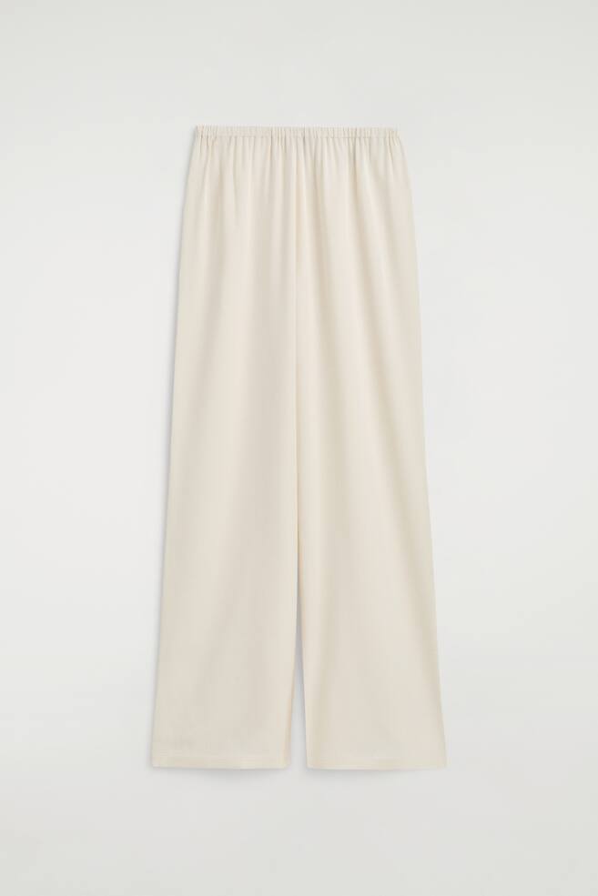 Elasticated crepe straight-leg trousers in a light cream colour are shown from the front, highlighting a gathered elasticated waistband and a relaxed silhouette. The fluid fabric drapes smoothly to a clean, straight hem. - 1