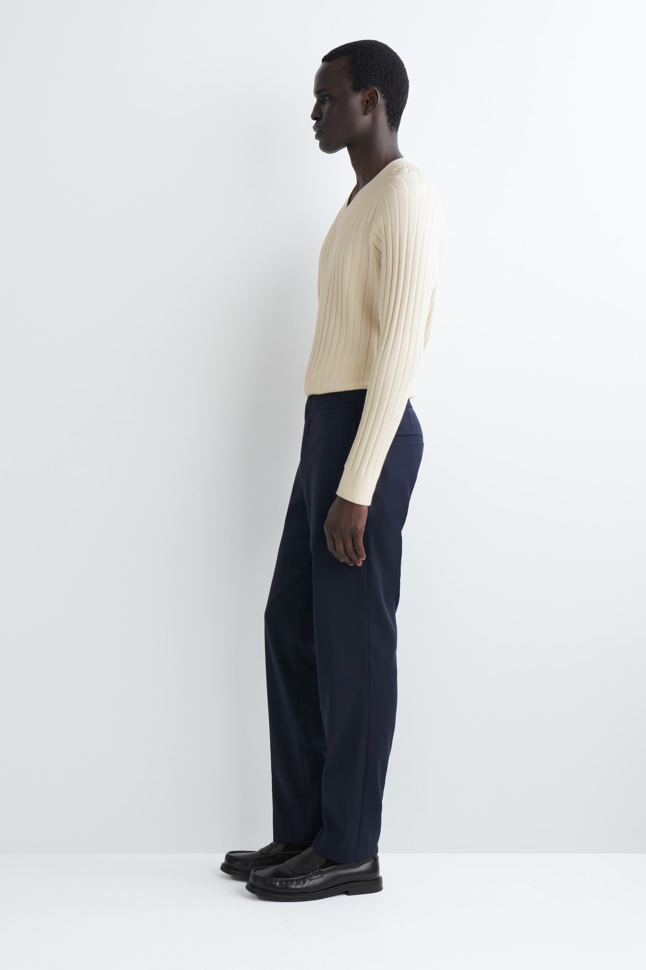 Vezi imaginea mai mare: Pantalonii negri slim sunt purtați de o persoană, văzuți din stânga, având o formă croită și elegantă care cade lin până la glezne. Aceștia sunt asortați cu un top de culoare deschisă și pantofi închiși la culoare.