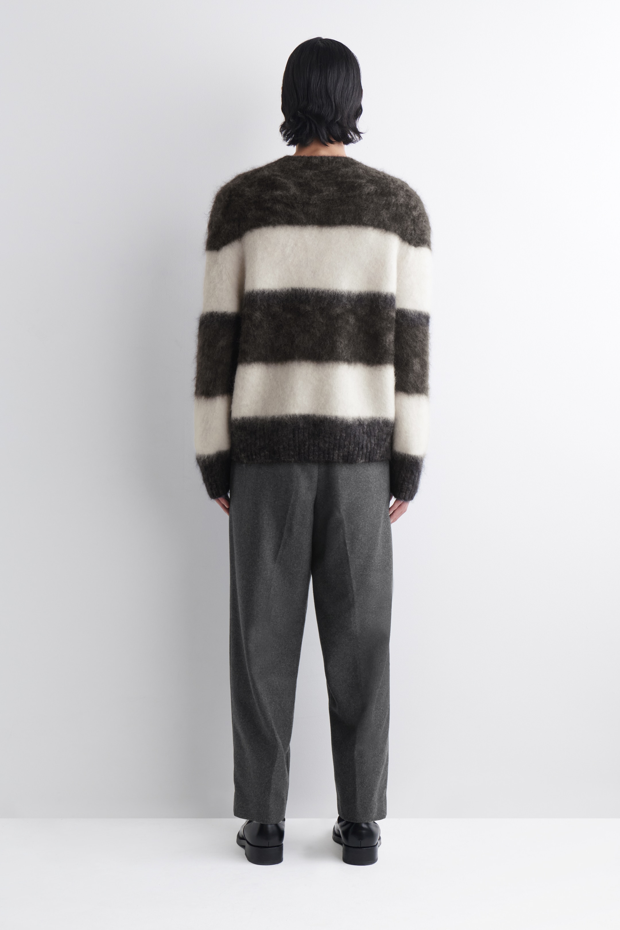 Agrandir l'image: Un pull à rayures horizontales floues en marron foncé et blanc cassé est montré de dos, avec une coupe décontractée, un col rond, et des poignets et un ourlet côtelés. Un pantalon gris foncé à jambes droites est porté en dessous.