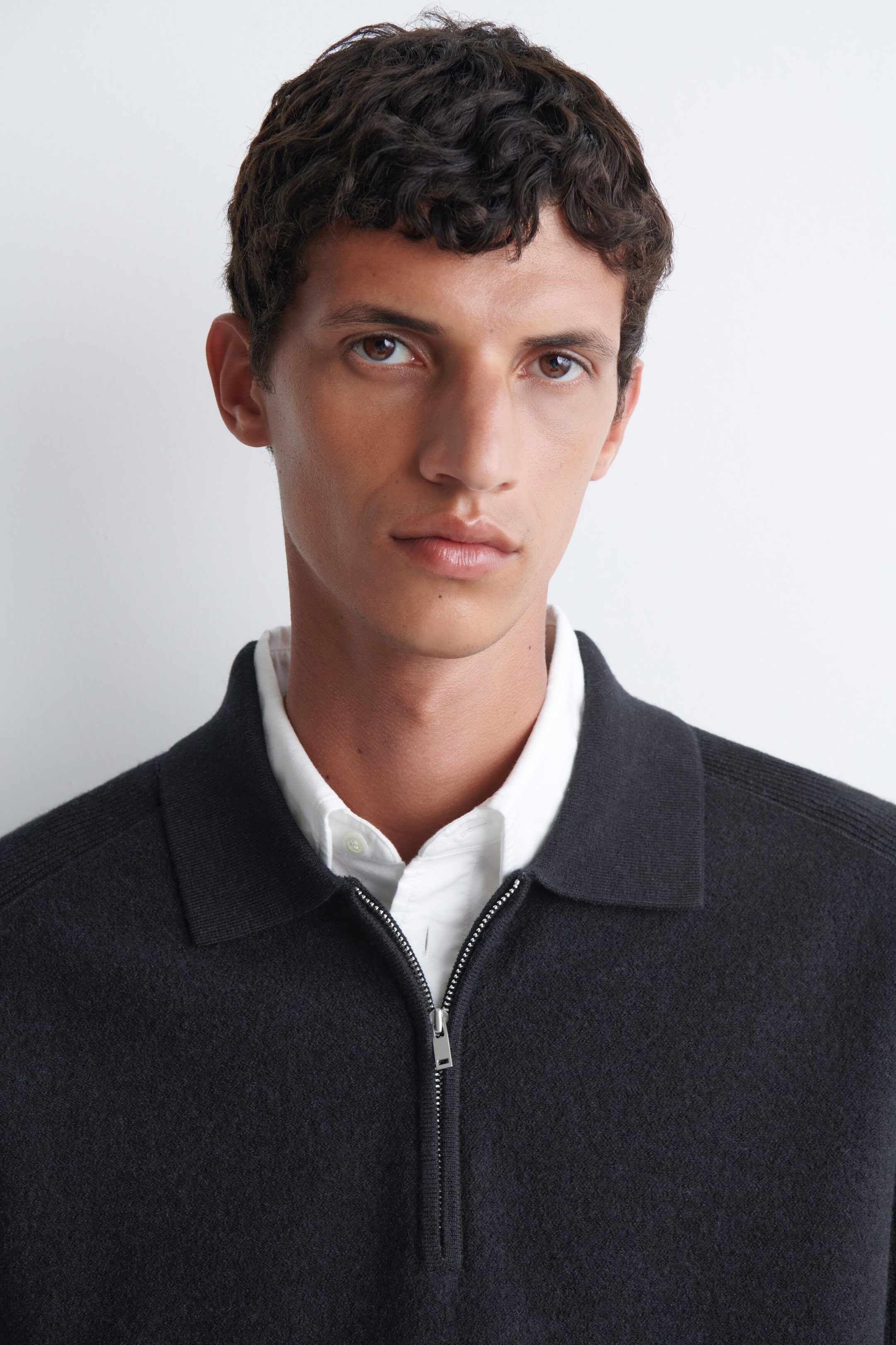 A paneled boiled-wool zip-up jumper in dark grey is being worn by the model. The jumper features a classic collar and a silver-tone half-zip closure, which is partially open to reveal a white collared shirt layered underneath. A paneled boiled-wool zip-up jumper in dark grey is being worn by the model. The jumper features a classic collar and a silver-tone half-zip closure, which is partially open to reveal a white collared shirt layered underneath.