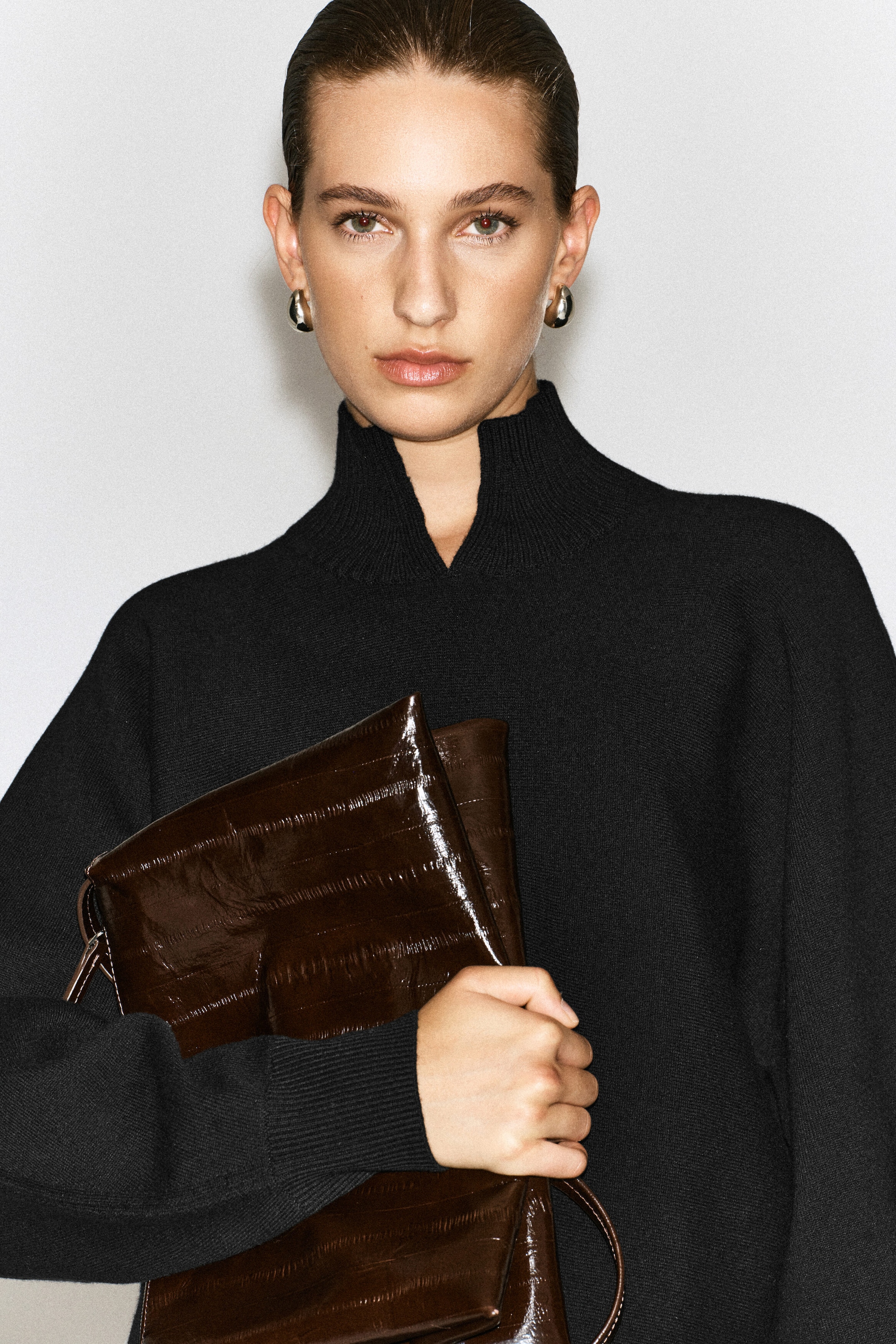Un chandail noir en laine bouillie à col cheminée, doté d’un col montant avec une découpe en V à l’avant et de poignets côtelés, est porté par le mannequin. Le mannequin tient un sac en cuir texturé brun foncé brillant contre le devant du chandail. Un chandail noir en laine bouillie à col cheminée, doté d’un col montant avec une découpe en V à l’avant et de poignets côtelés, est porté par le mannequin. Le mannequin tient un sac en cuir texturé brun foncé brillant contre le devant du chandail.