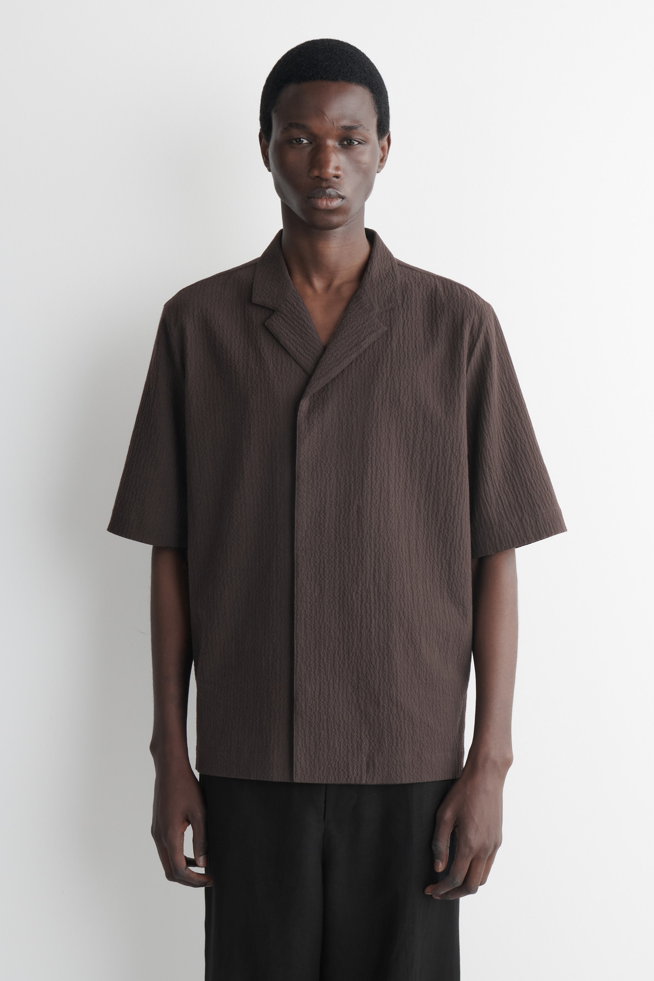 Se større billede: En brun kortærmet skjorte præsenteres forfra, med et tekstureret stof, en camp-krave og en åben V-hals placket.