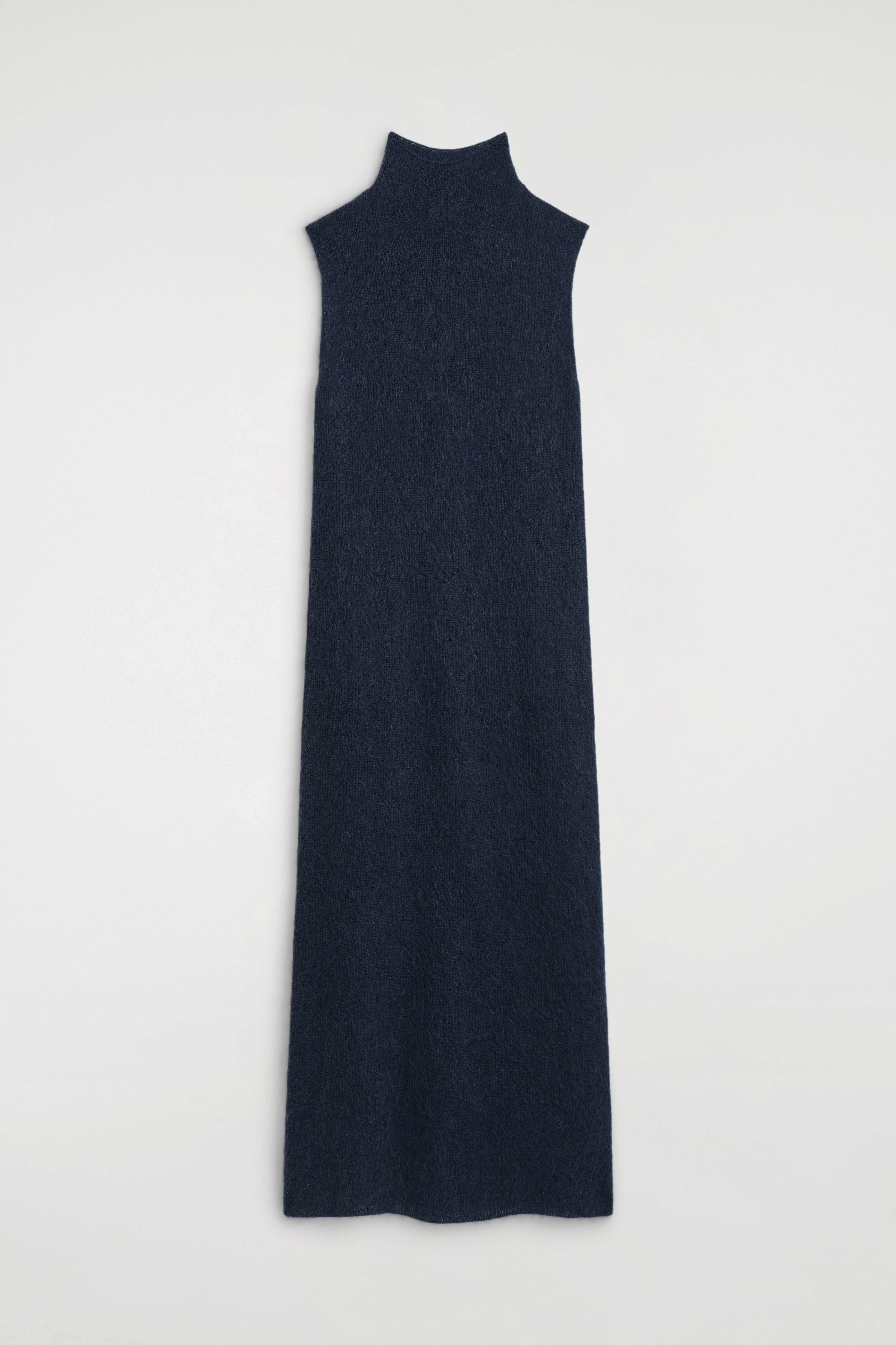 En bÃ¸rstet kjole med funnel-neck i mÃ¸rk navy bÃ¦res af modellen og har en Ã¦rmelÃ¸s, lige midi-silhuet. Strikkjolen er stylet med en mÃ¸rkegrÃ¥ sweater bundet omkring ÑÐ°Ð»jen og matches med en sort skuldertaske og sorte loafers.