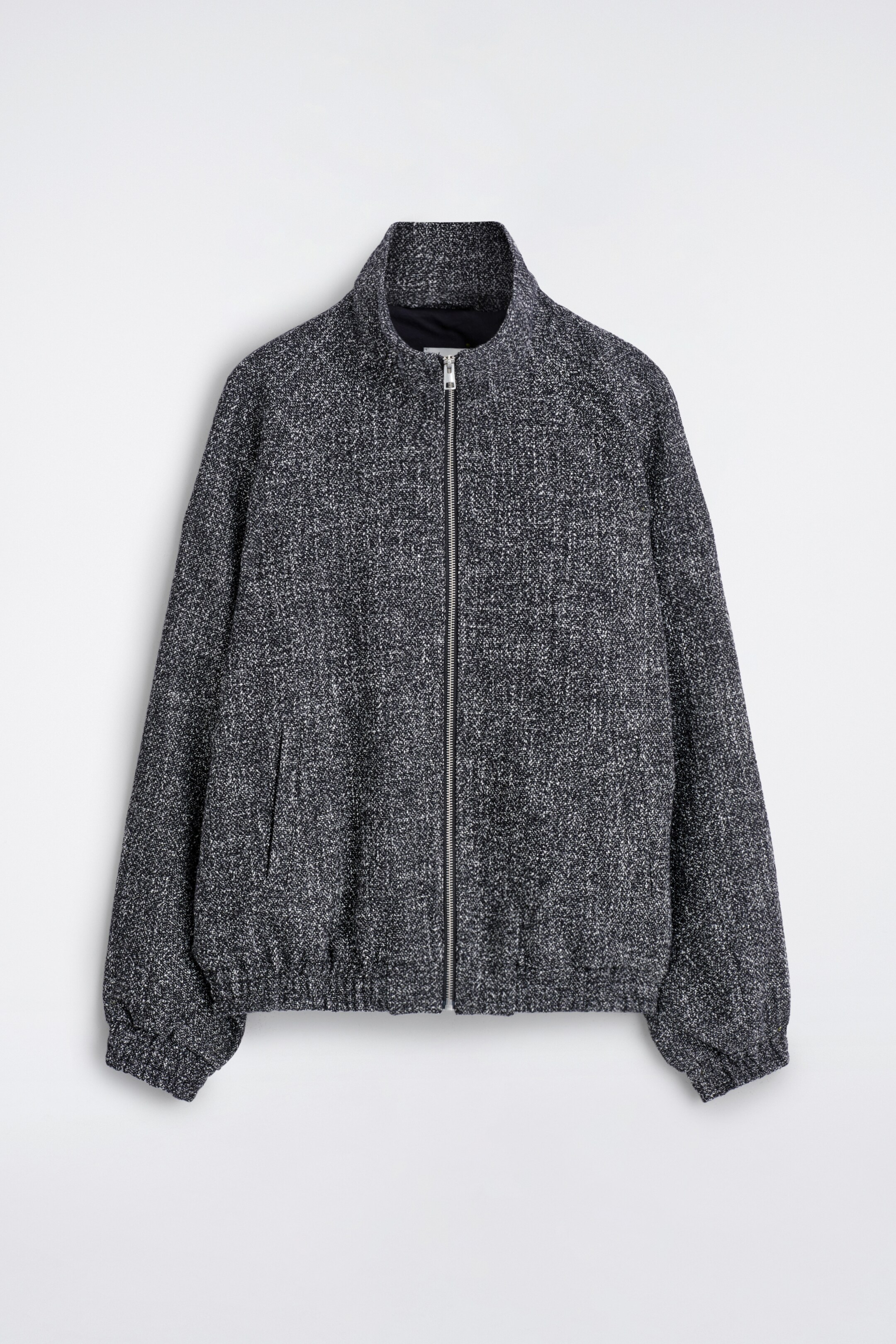 Grösseres Bild ansehen: Die Trainingsjacke wird von vorne präsentiert und zeichnet sich durch eine dunkelgraue Tweed-Textur mit weißen Sprenkeln, einen durchgehenden Frontreißverschluss, einen Trichterkragen, Raglanärmel, zwei dezente Leistentaschen sowie elastische Bündchen und einen elastischen Saum aus.