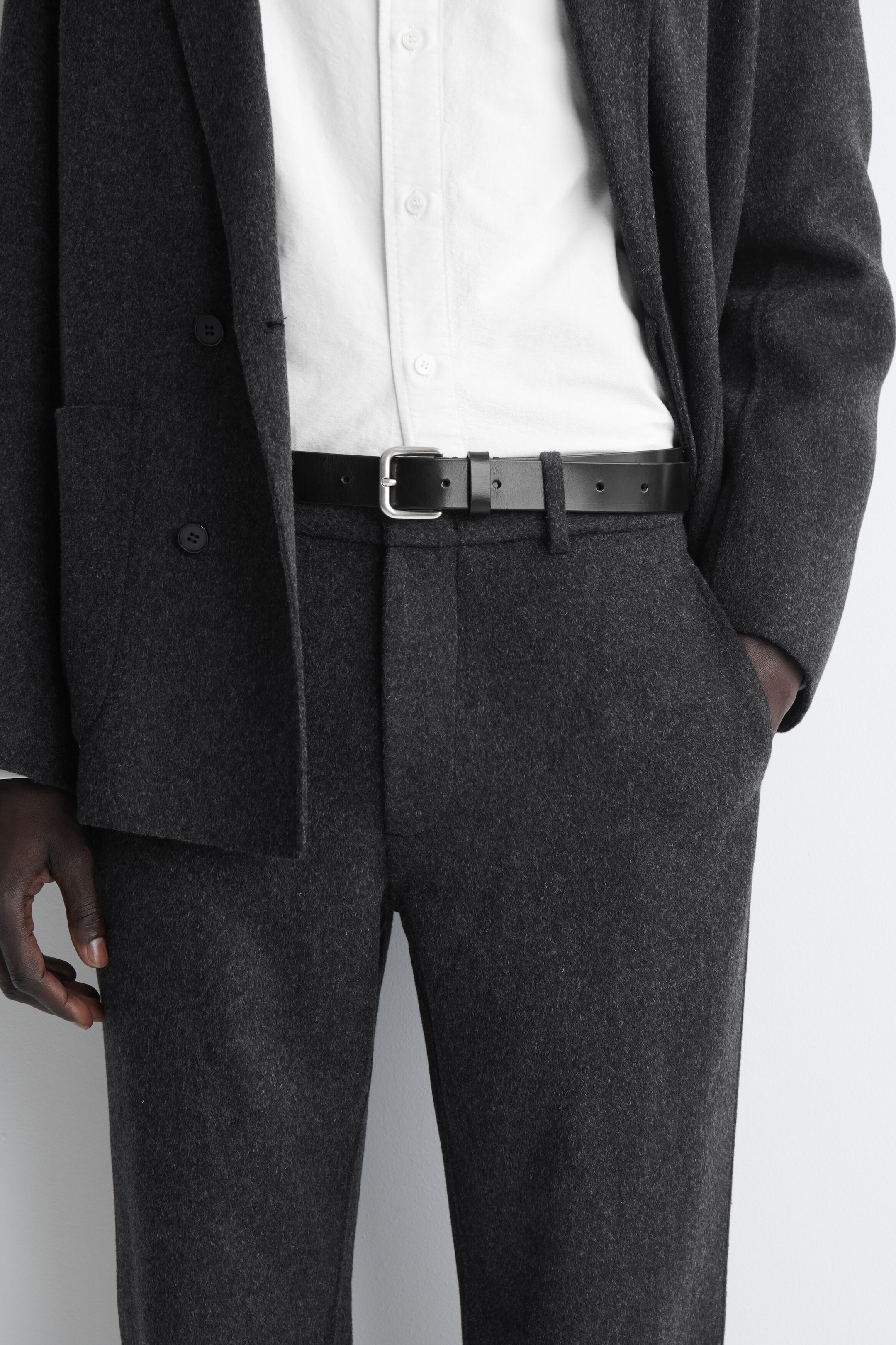These dark grey wool-blend trousers are shown from the front, featuring belt loops styled with a black leather belt and side slip pockets. They are worn as part of a suit with a matching dark grey blazer and a tucked-in white button-up shirt. These dark grey wool-blend trousers are shown from the front, featuring belt loops styled with a black leather belt and side slip pockets. They are worn as part of a suit with a matching dark grey blazer and a tucked-in white button-up shirt.