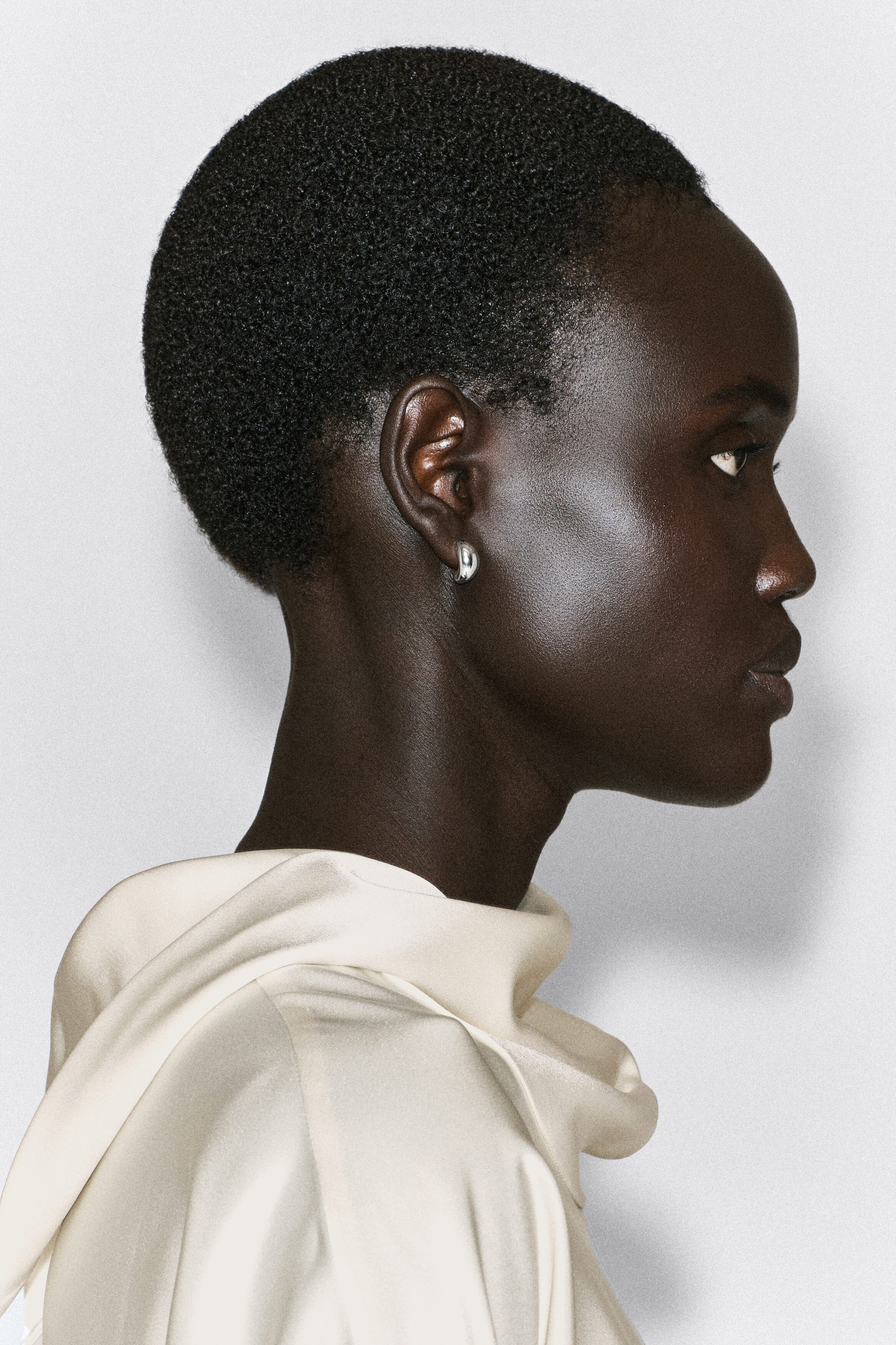 Une boucle d’oreille demi-créole sculpturale est portée au lobe de l’oreille d’un mannequin montré de profil, faisant face à droite, mettant en valeur sa forme volumineuse et incurvée ainsi que sa finition argentée hautement polie. Une boucle d’oreille demi-créole sculpturale est portée au lobe de l’oreille d’un mannequin montré de profil, faisant face à droite, mettant en valeur sa forme volumineuse et incurvée ainsi que sa finition argentée hautement polie.