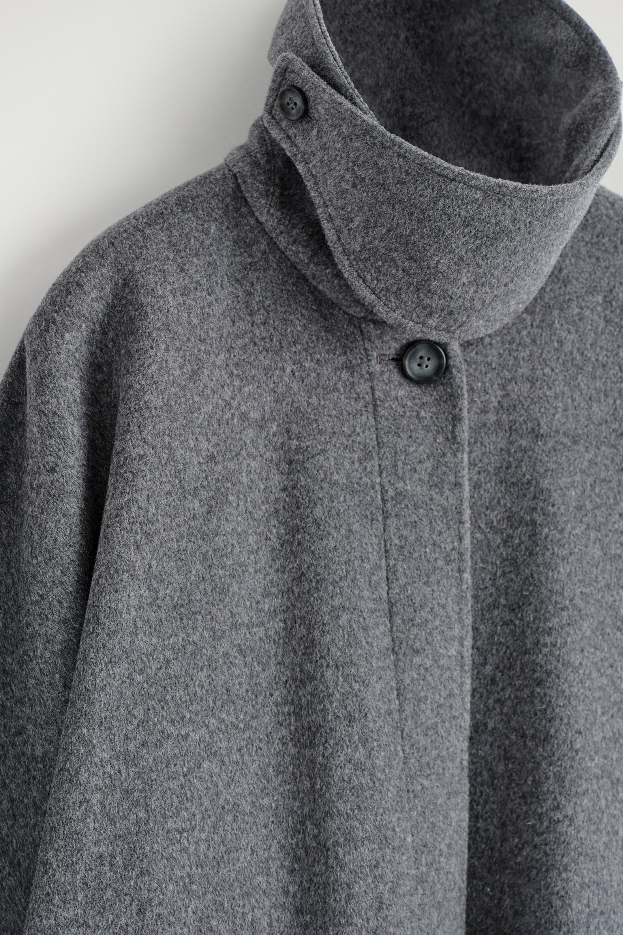 Agrandir l'image: Le Longline Double-Faced Wool Cape est présenté de FACE, fabriqué en tissu de laine gris texturé. Il présente un col entonnoir haut et droit avec une fermeture boutonnée latérale visible, et un bouton gris foncé sécurise la patte de boutonnage avant alors que le tissu de la cape se drape largement.