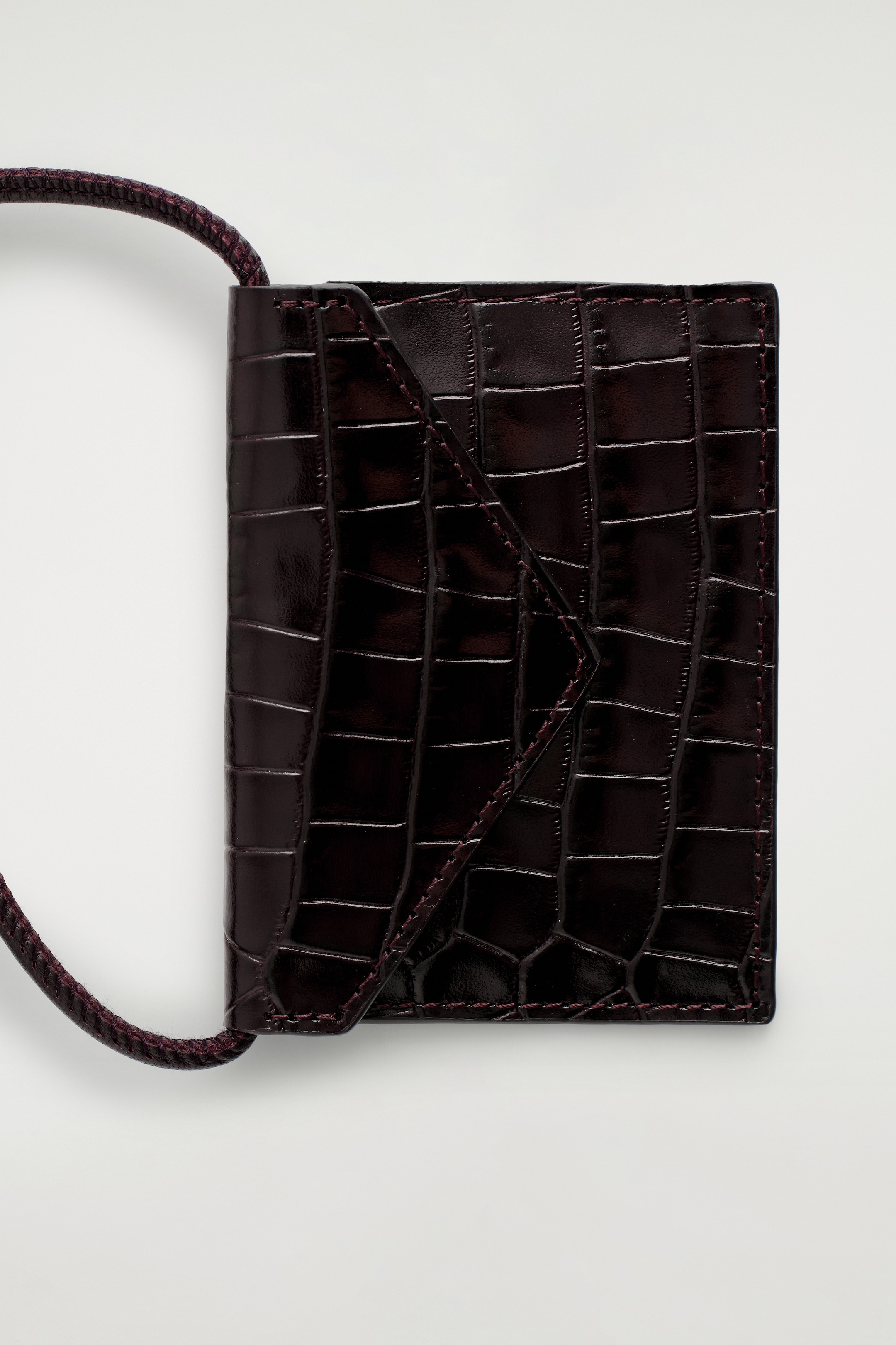 Grösseres Bild ansehen: Der CROC-EMBOSSED LEATHER CARDHOLDER wird von OBEN präsentiert, mit einem glänzenden dunkelburgunderroten Finish und einer krokogeprägten Textur. Es zeigt eine schräge Vorderklappe mit sichtbaren Nähten, und eine geflochtene Kordelschlaufe erstreckt sich von seiner linken Seite.