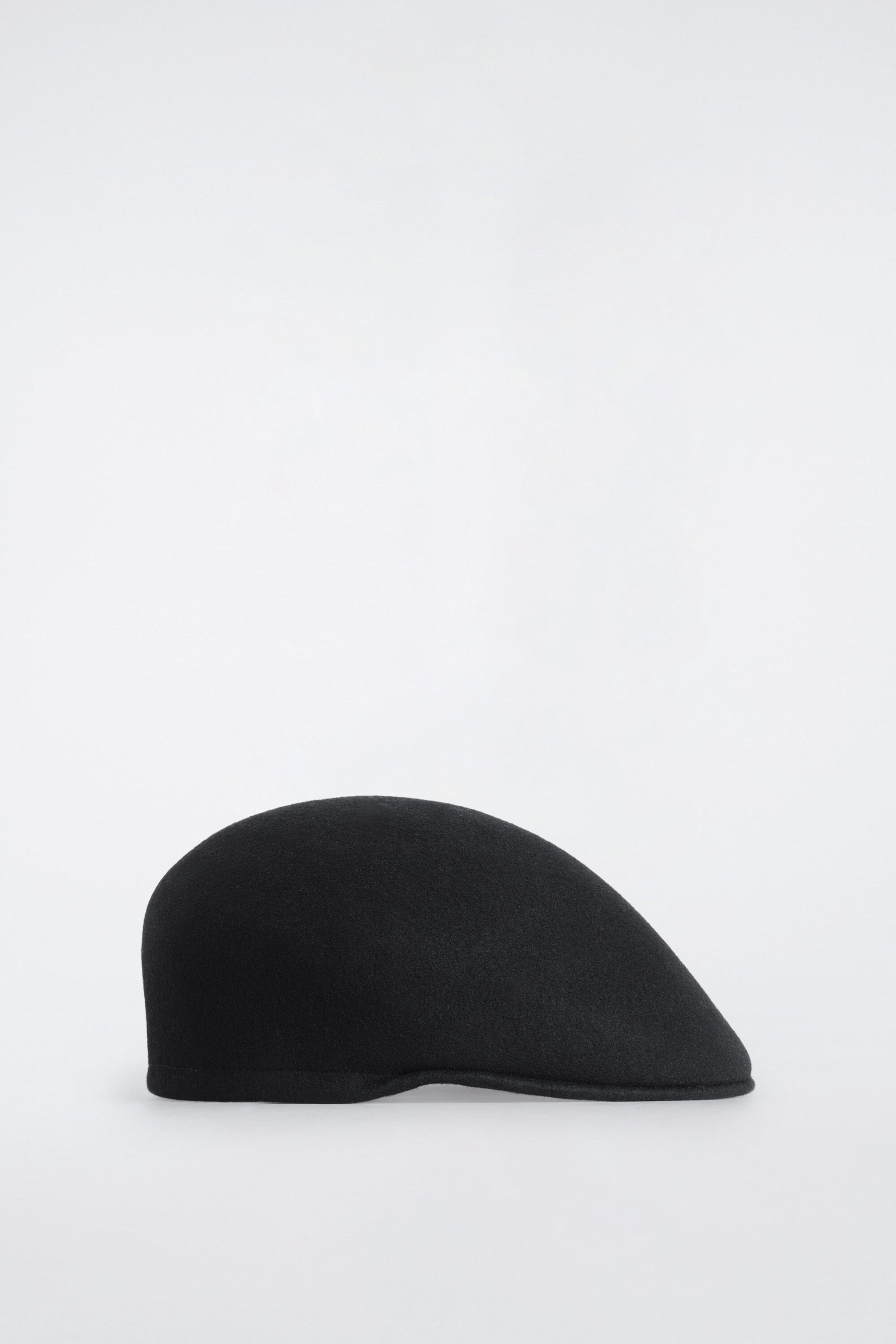Une casquette plate noire en laine bouillie texturée est présentée de profil, tournée vers la droite, mettant en valeur sa calotte lisse et arrondie ainsi que sa visière rigide intégrée. Une casquette plate noire en laine bouillie texturée est présentée de profil, tournée vers la droite, mettant en valeur sa calotte lisse et arrondie ainsi que sa visière rigide intégrée.