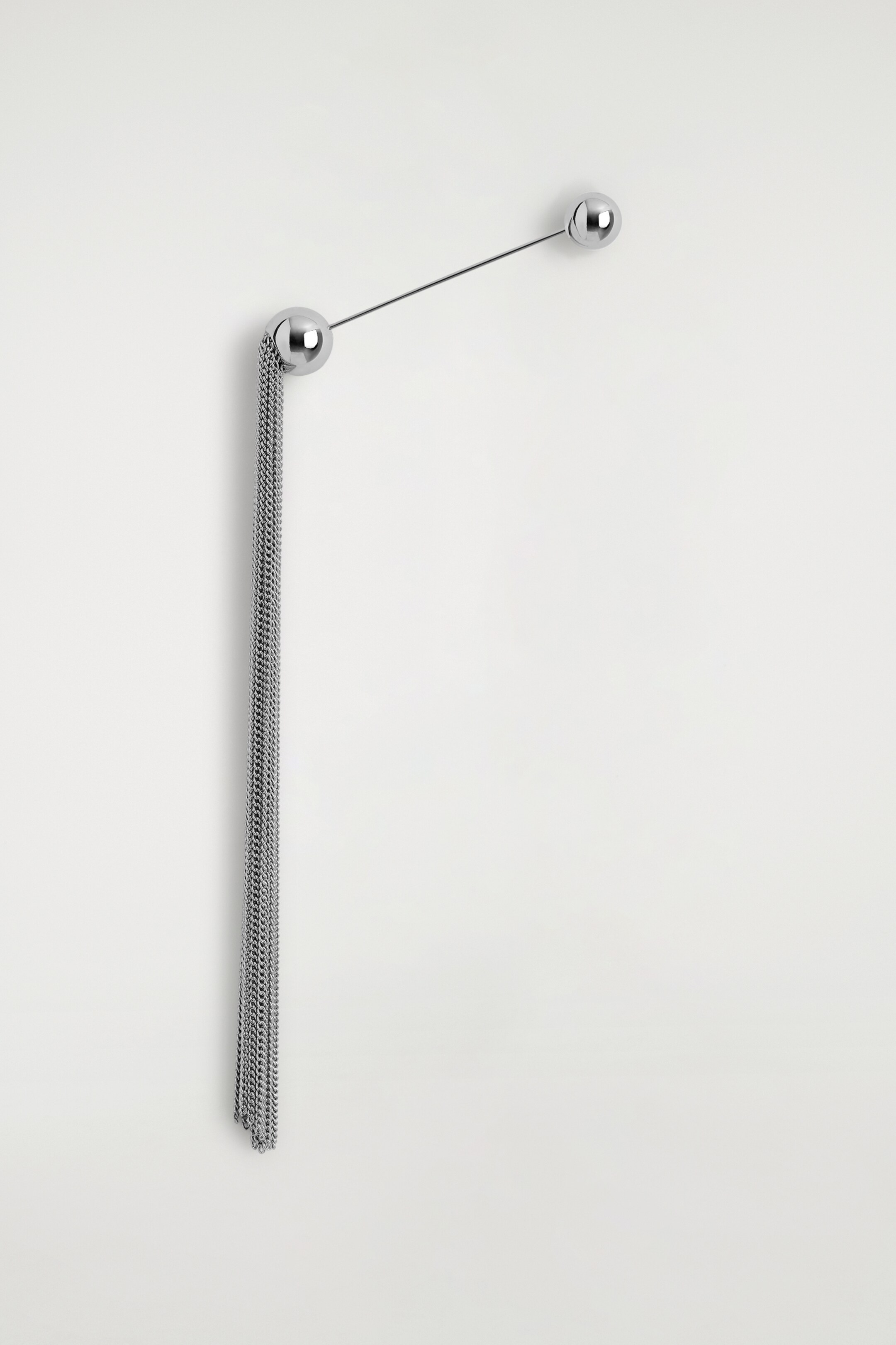 Ver imagen más grande: Un solo pendiente de tono plateado está mostrando una vista FRONTAL de su diseño, con dos bolas metálicas esféricas y pulidas conectadas por una varilla delgada. Numerosas cadenas finas están colgando verticalmente del balón más grande.