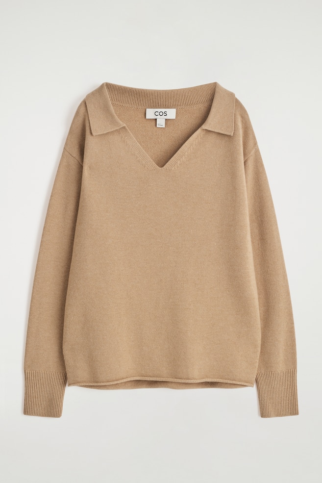 Se muestra un suéter de punto color beige desde el frente, con un cuello polo con escote en V y mangas largas con puños acanalados. - 1