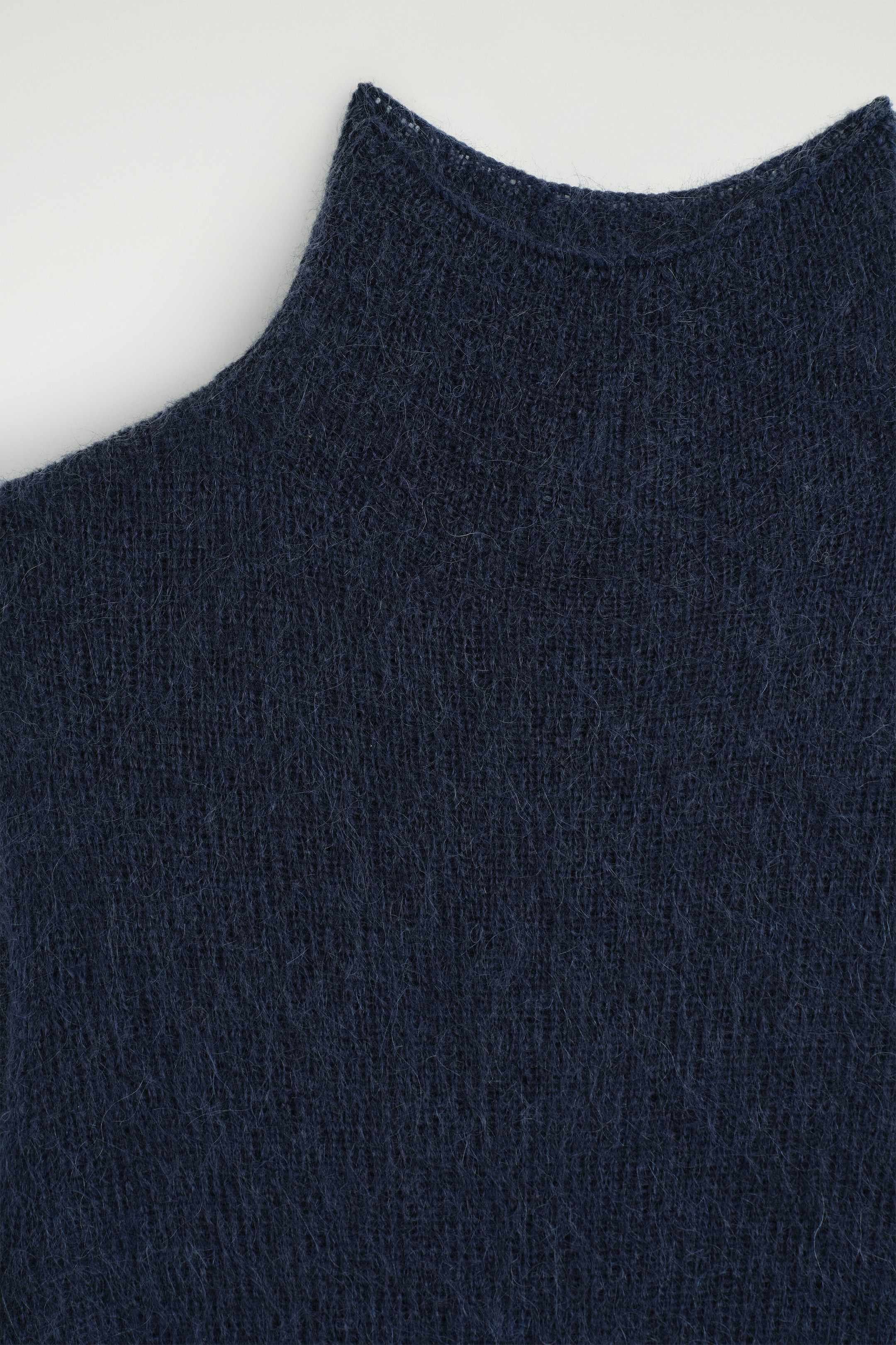 A close-up of the brushed funnel-neck dress in dark navy blue shows off its soft, fuzzy knit texture and the structured shape of the funnel neckline from the front.