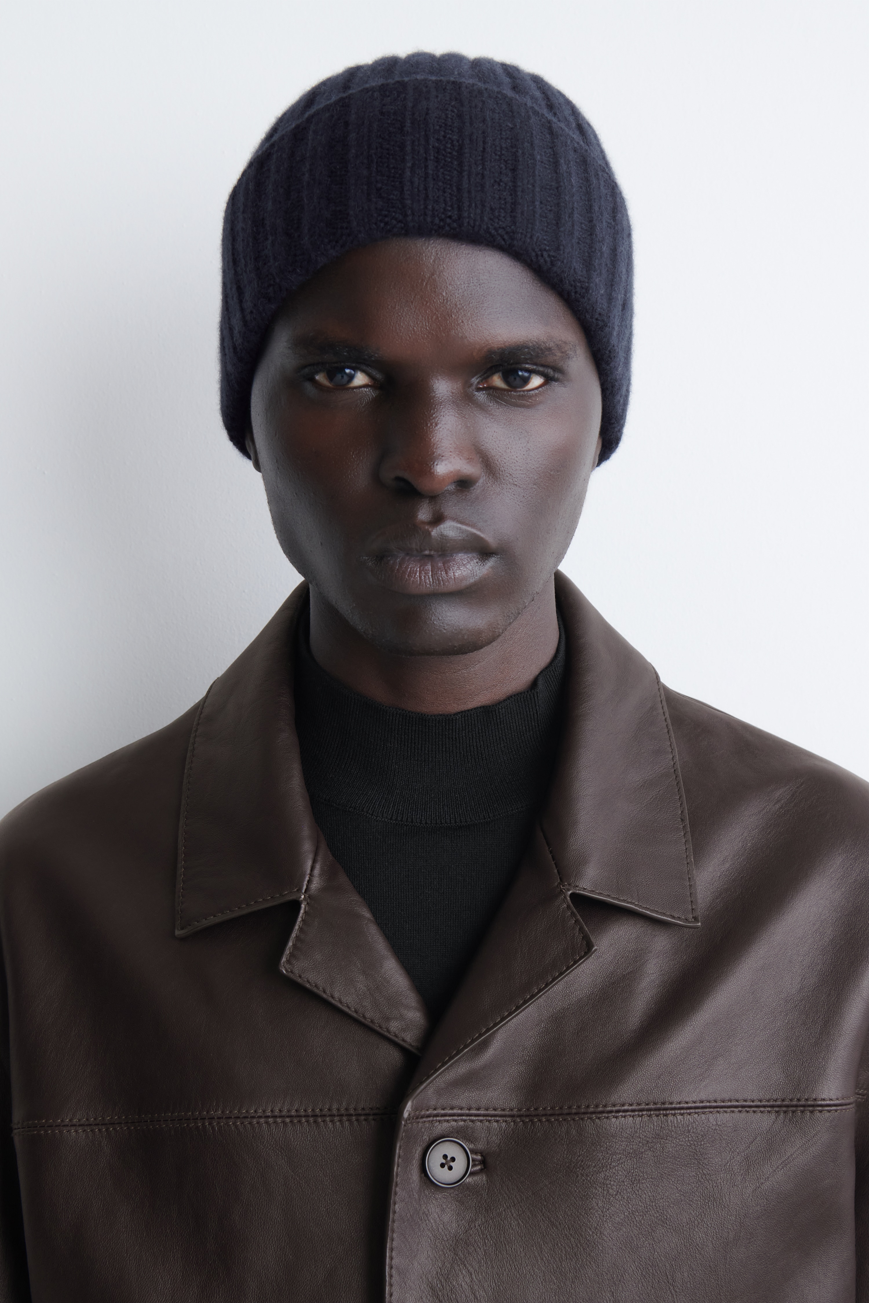 A chunky ribbed cashmere beanie in dark navy blue is shown from the front, highlighting its thick vertical ribbed knit construction. The beanie features a wide, folded-up cuff and a rounded crown structure.
