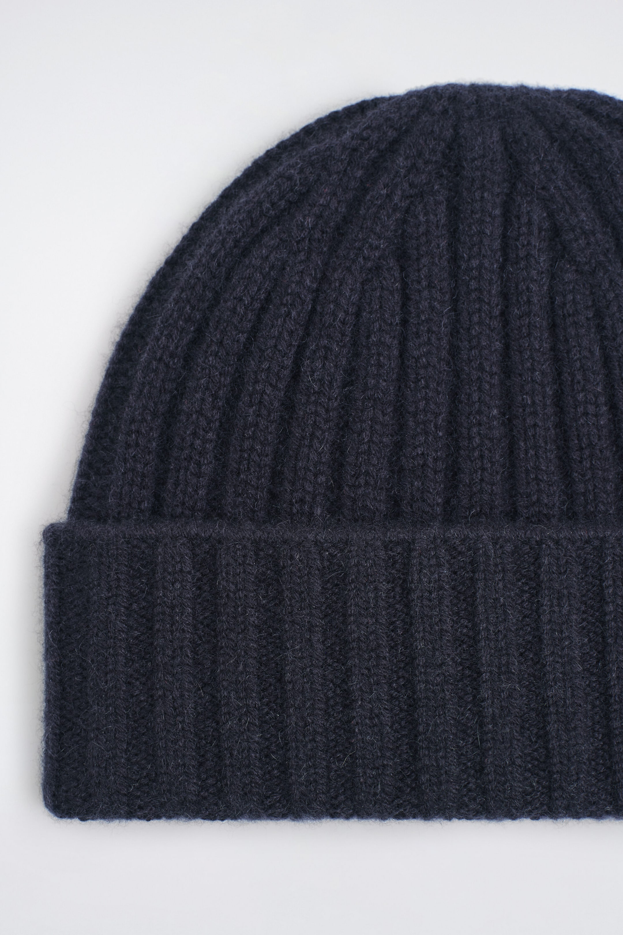 The chunky ribbed cashmere beanie is showing off its dark navy blue color and soft, fuzzy texture in a close-up front view. It features a vertical rib-knit pattern and a thick fold-over cuff.