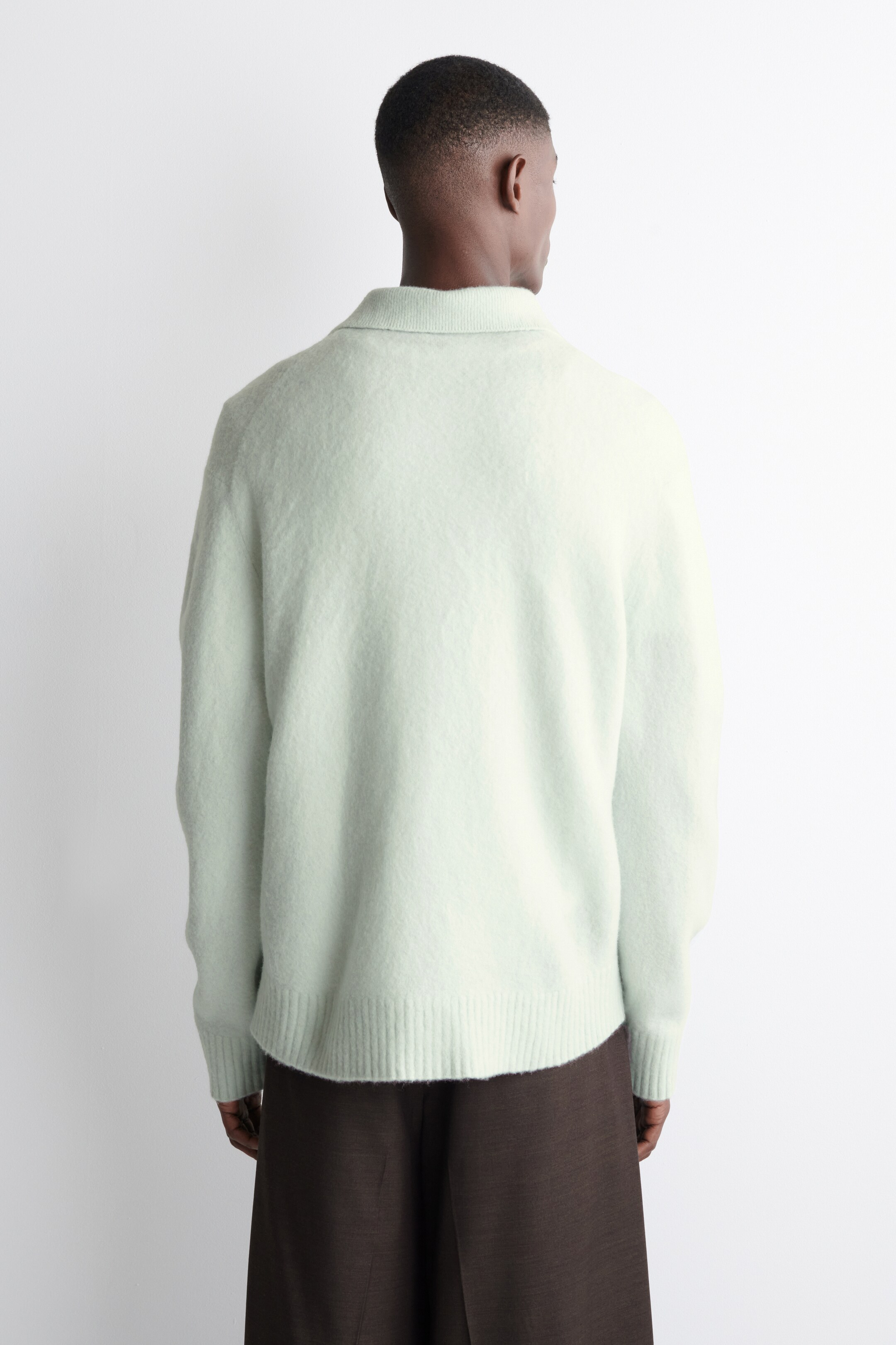 Visualizza immagine più grande: Un maglione soffice verde chiaro viene osservato dal retro, mostrando un colletto a punte dritte, un orlo a costine e polsini a costine.