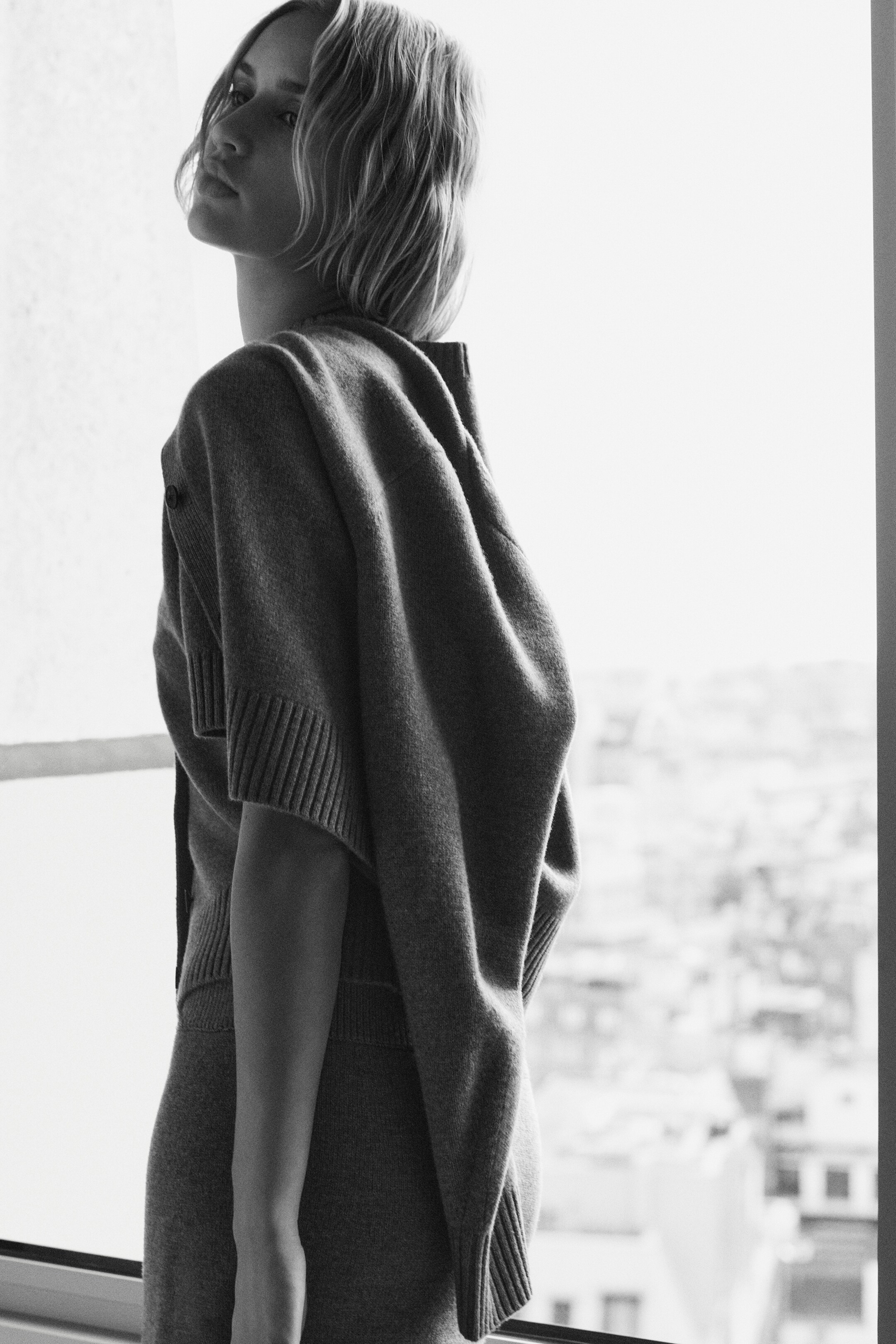 View larger image: A mole-colored merino wool short-sleeved cropped cardigan, featuring ribbed cuffs and a tonal button, is being draped over the shoulders. A matching mole-colored merino wool mini skirt with ribbed trims is also visible.