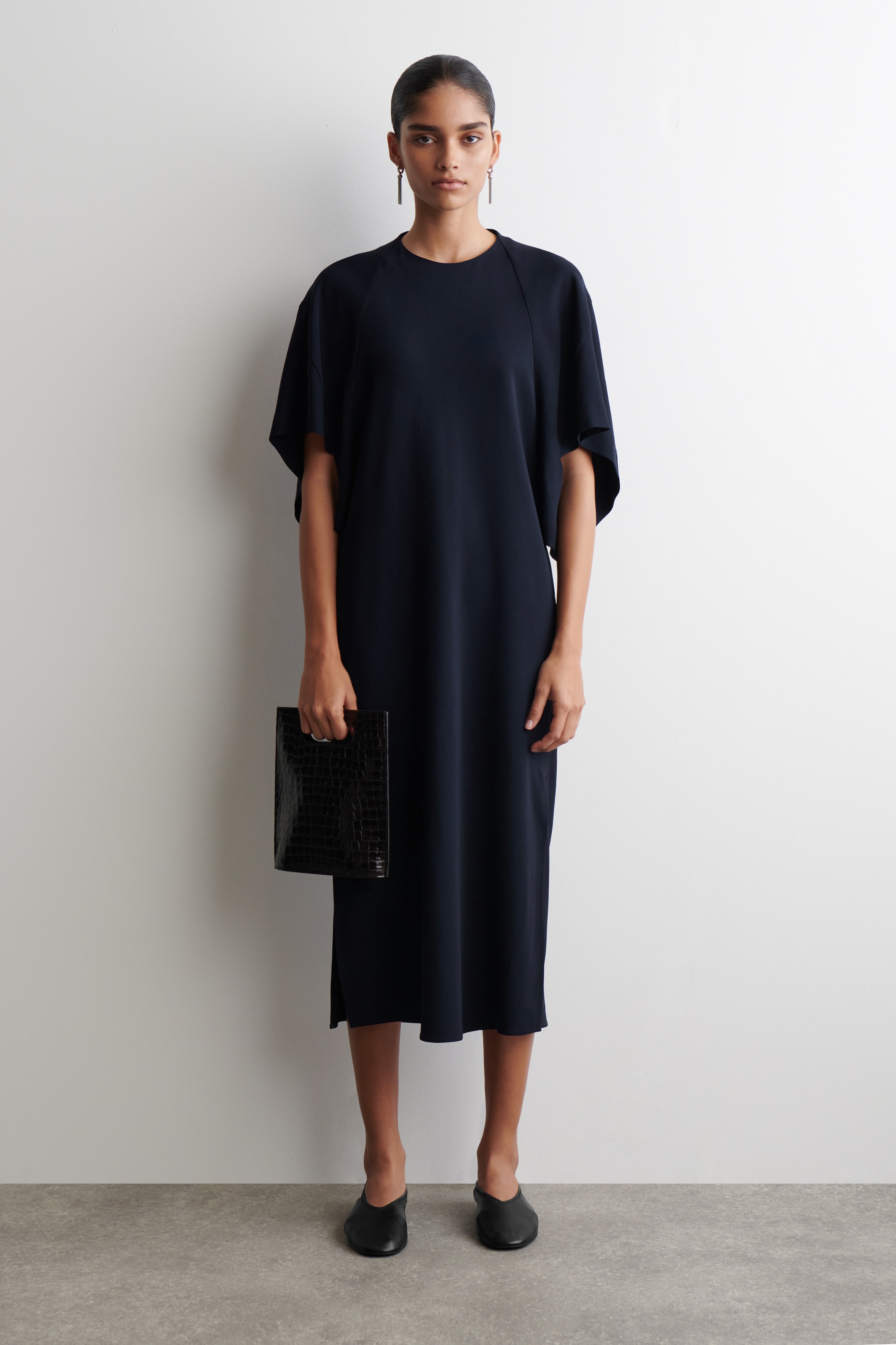 Grösseres Bild ansehen: Ein marineblaues Midikleid wird von vorne präsentiert, mit einem runden Ausschnitt, weiten, fließenden Dolman-Ärmeln und einem lockeren, geraden Schnitt, der bis zur Midilänge reicht.