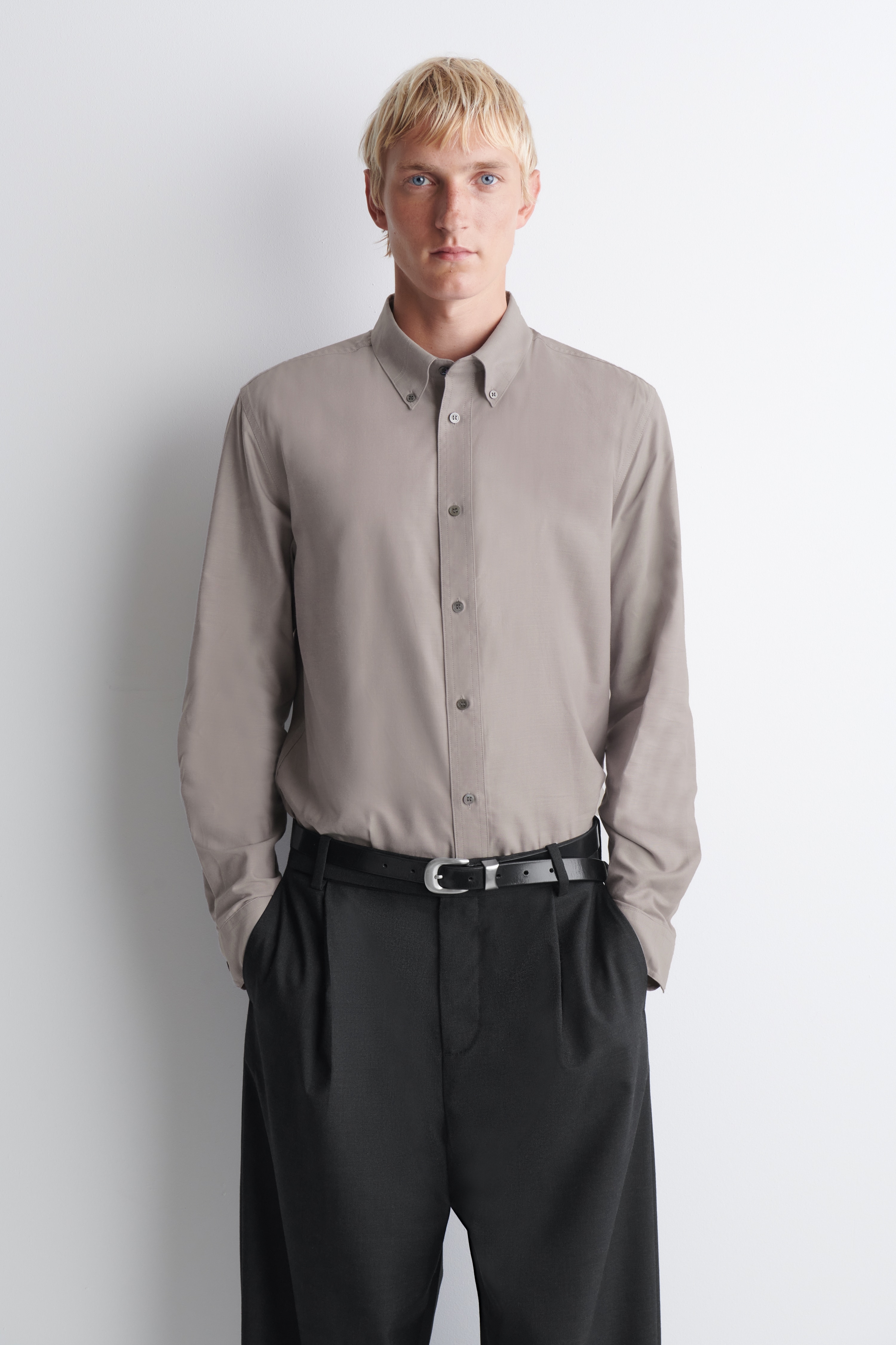 Una camisa Oxford cepillada de cuello abotonado en un tono topo apagado aparece colgada en una vista frontal, mostrando su estructura limpia y su corte regular. La camisa presenta un clÃ¡sico cuello abotonado, una botonera central, mangas largas con puÃ±os abotonados y un bajo sutilmente redondeado.