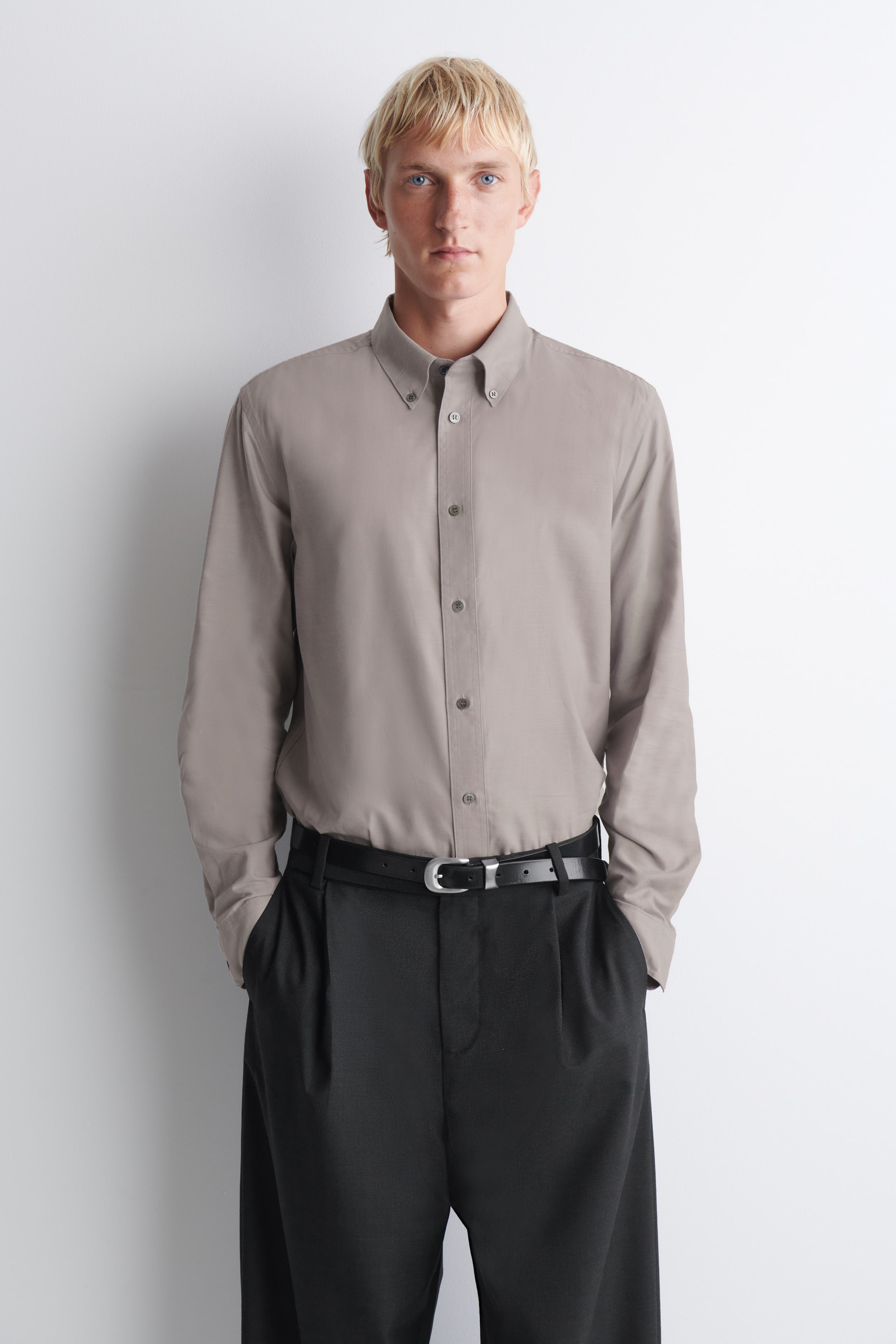 Ver imagen más grande: Una camisa oxford de tejido cepillado con cuello abotonado en un tono topo apagado se lleva de frente, metida por dentro de un pantalón negro de pinzas con cinturón negro. La camisa presenta un cuello abotonado clásico, una botonadura tonal y mangas largas.