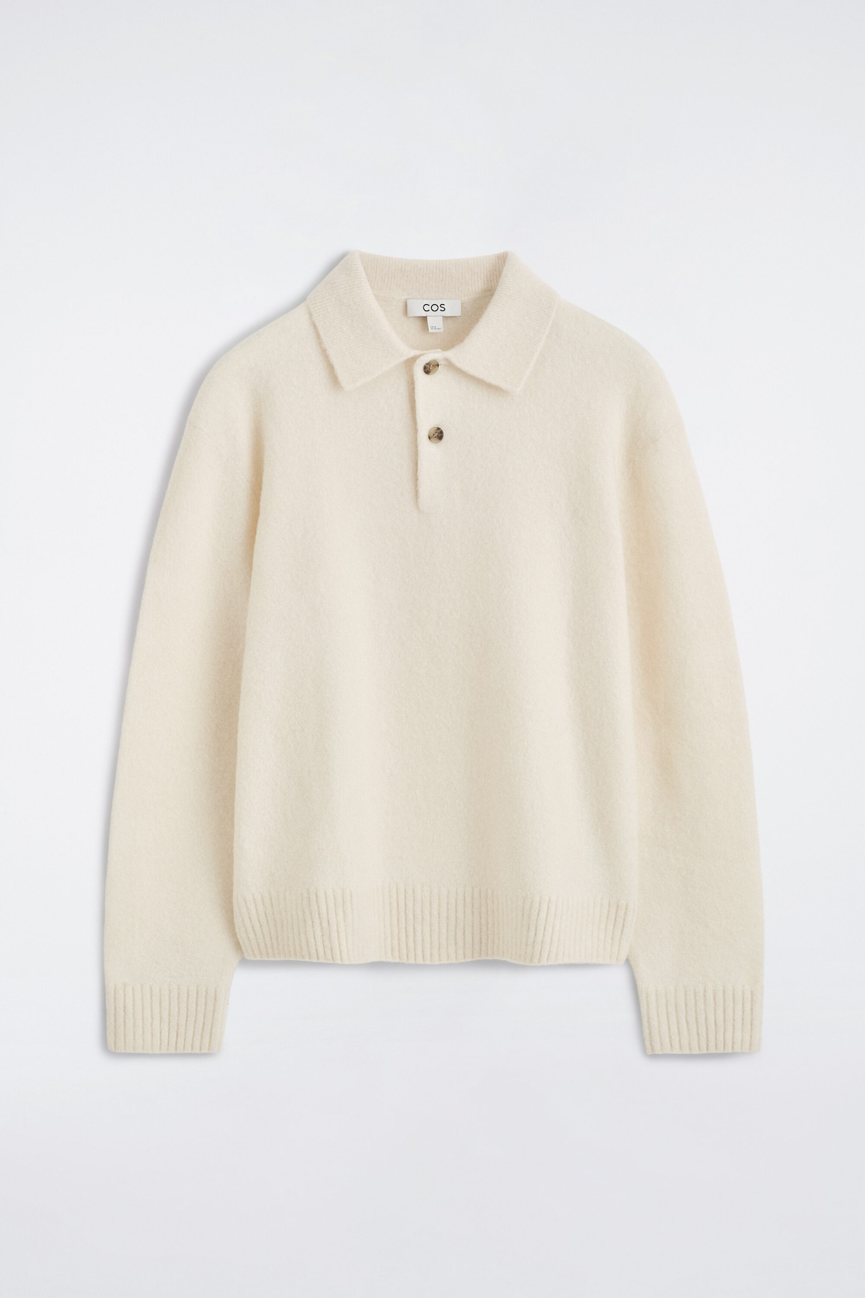 A cream-colored brushed wool polo shirt is shown from the front, featuring a classic spread collar and a partial placket with two buttons. The long-sleeved garment has a soft, textured finish with ribbed cuffs and a ribbed hem.