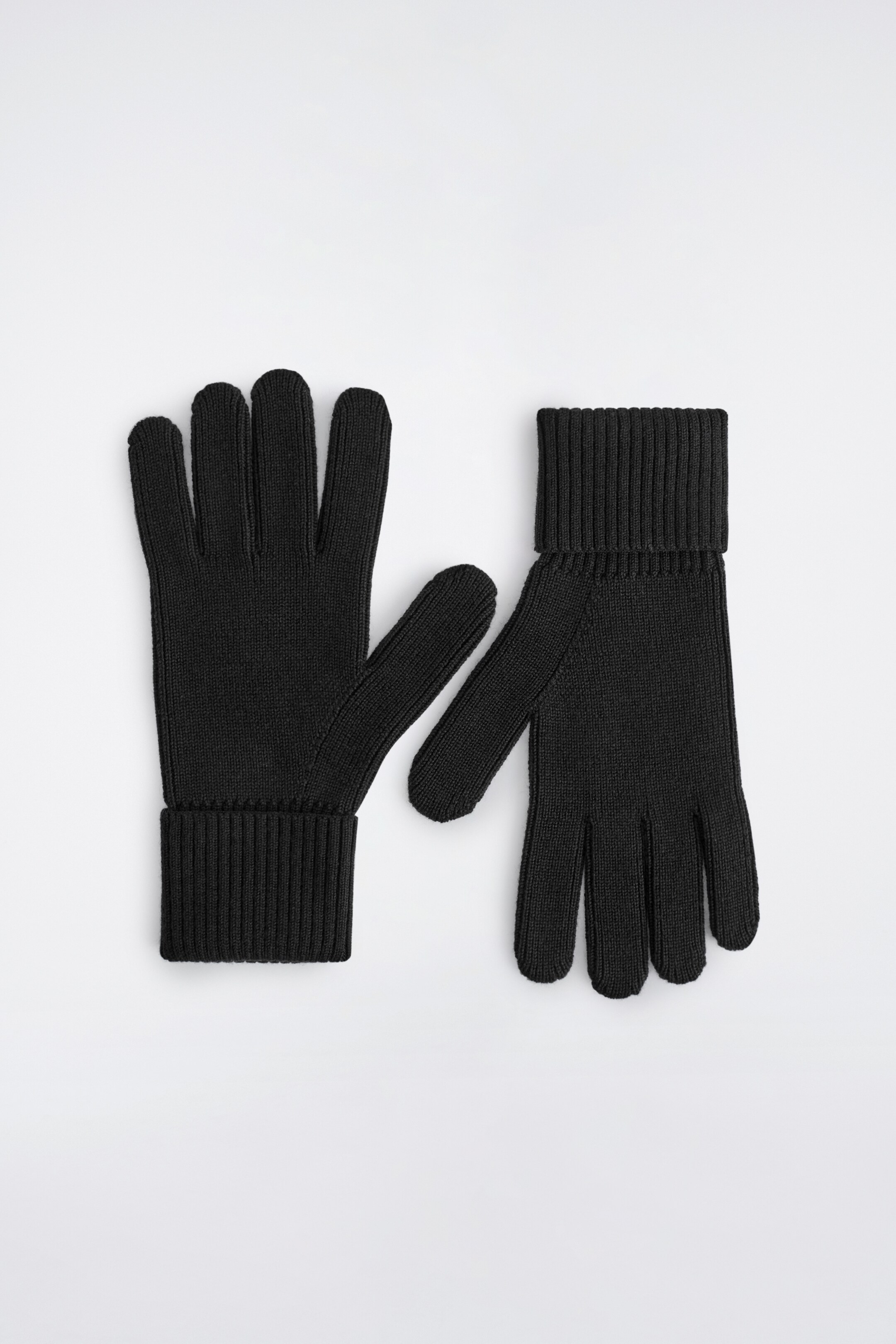 Agrandir l'image: Une paire de gants noirs en maille côtelée est affichée à plat, avec un gant présentant sa paume et l'autre son dos. Les deux gants présentent des poignets côtelés repliés.