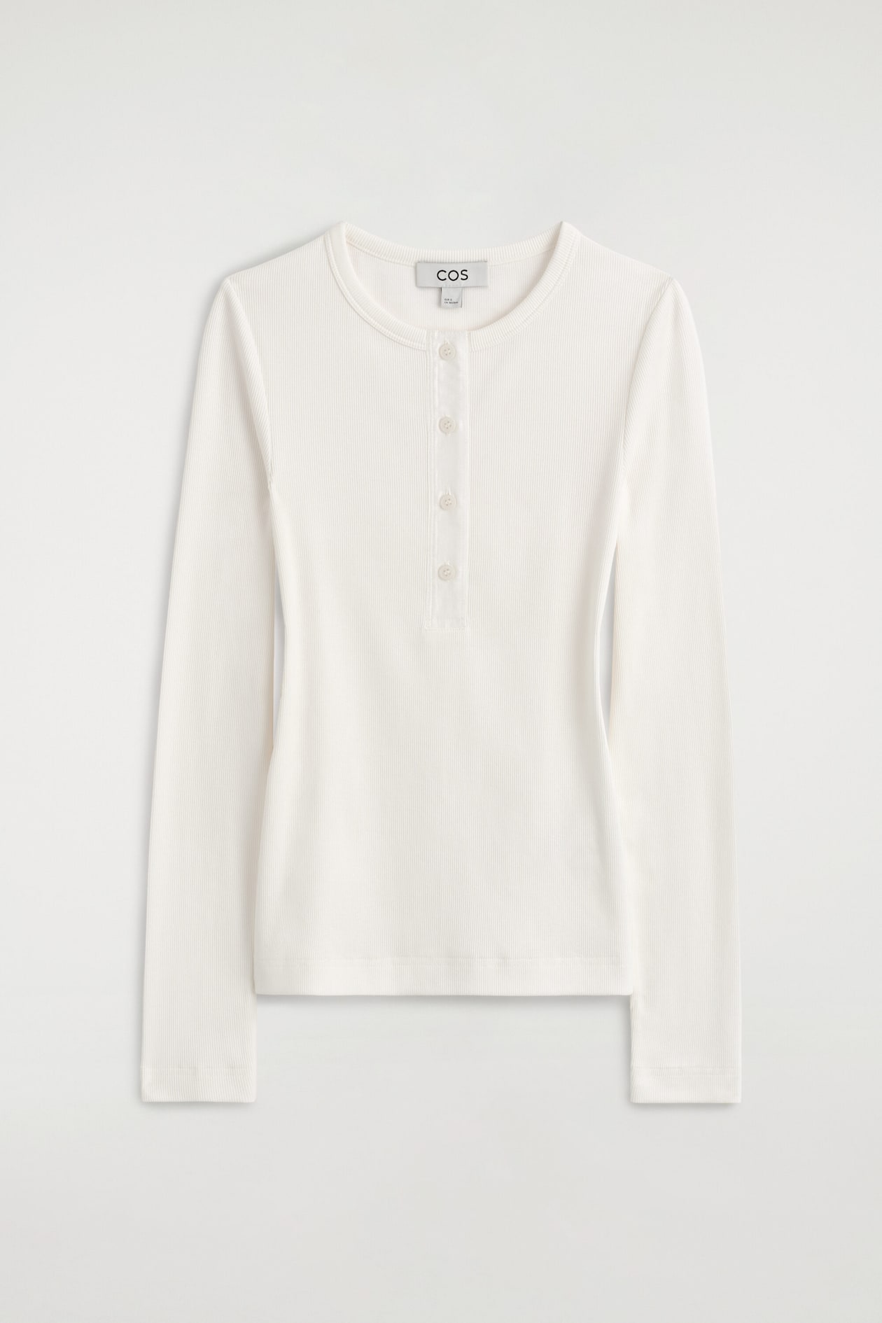 This ribbed cotton henley top is shown from the front, featuring a fine ribbed texture in an off-white shade. It has long sleeves, a crew neckline, and a partial front placket with four tone-on-tone buttons.